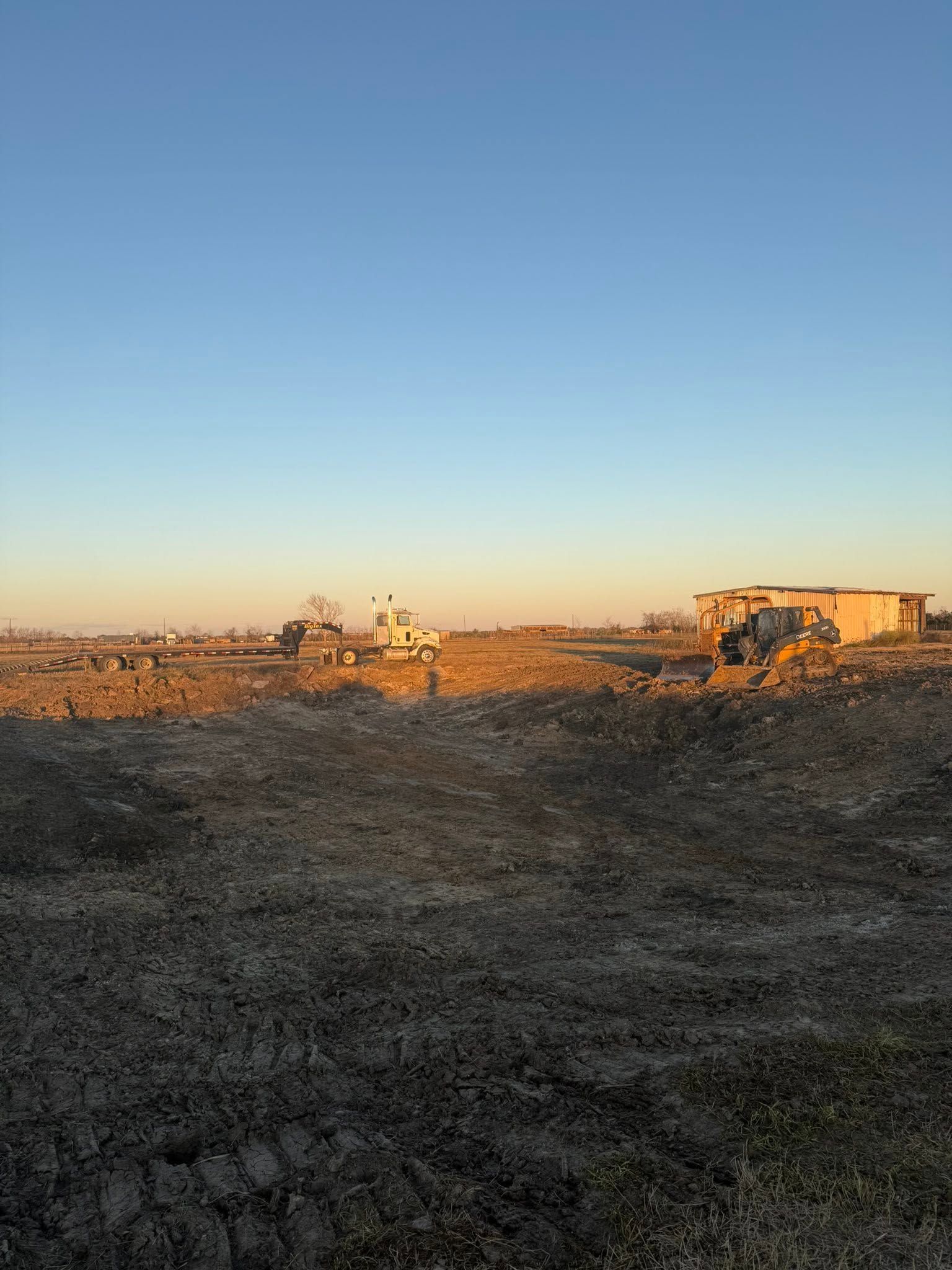 Open field at sunset with distant buildings and construction equipment under a clear blue sky
