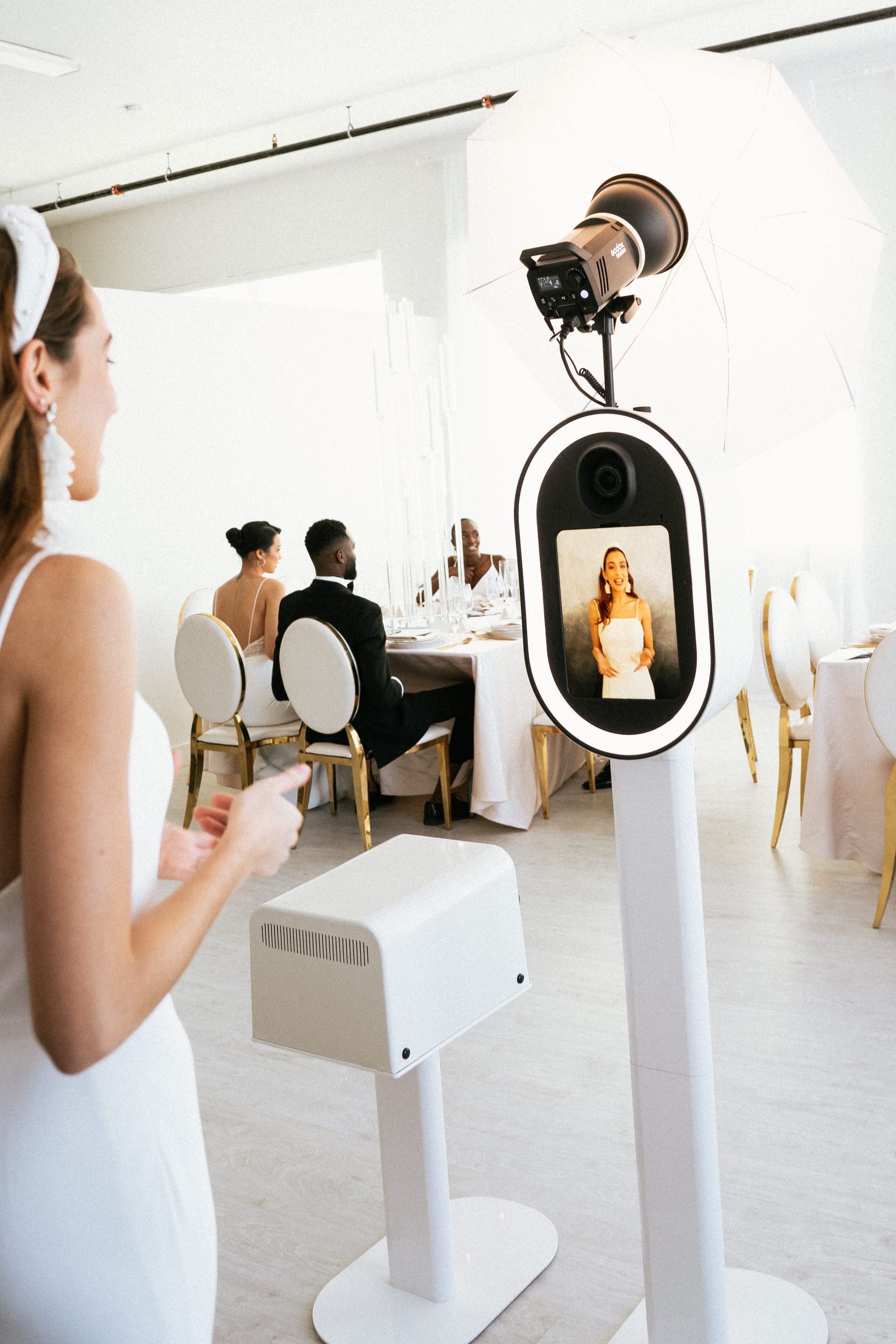 A woman poses for a photo booth at a wedding reception. People seated at a table in the background.
