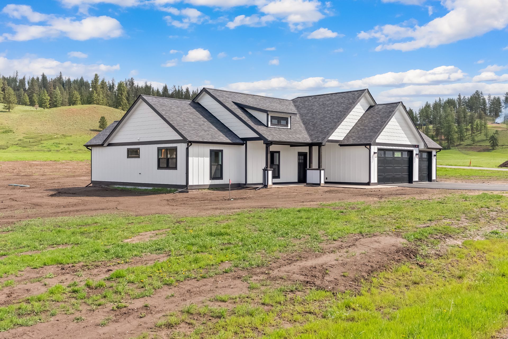 White modern house on a dirt lot with a gray roof under a cloudy blue sky.