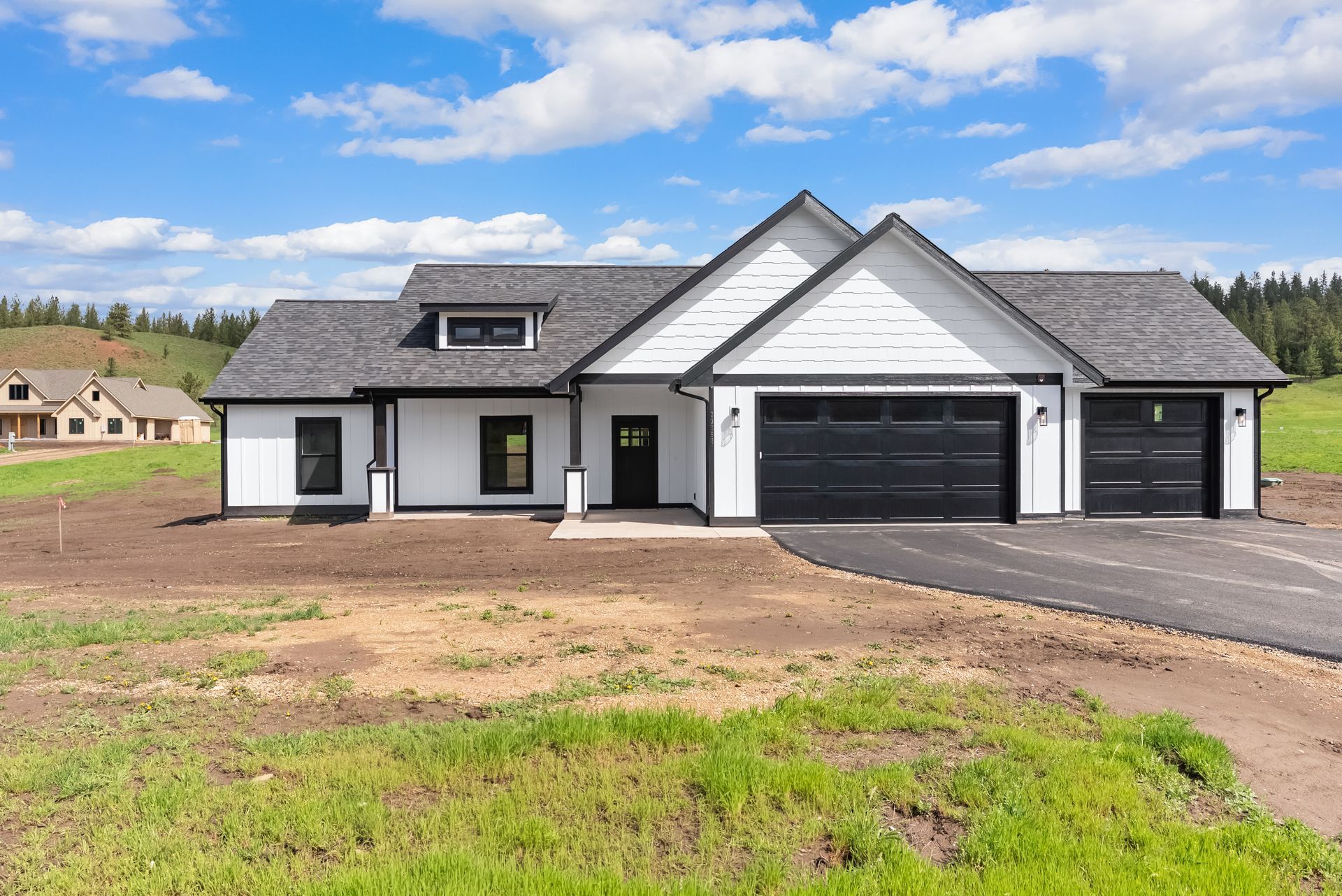 Modern white-and-gray single-story house with a three-car garage on a bare lot under a partly cloudy sky
