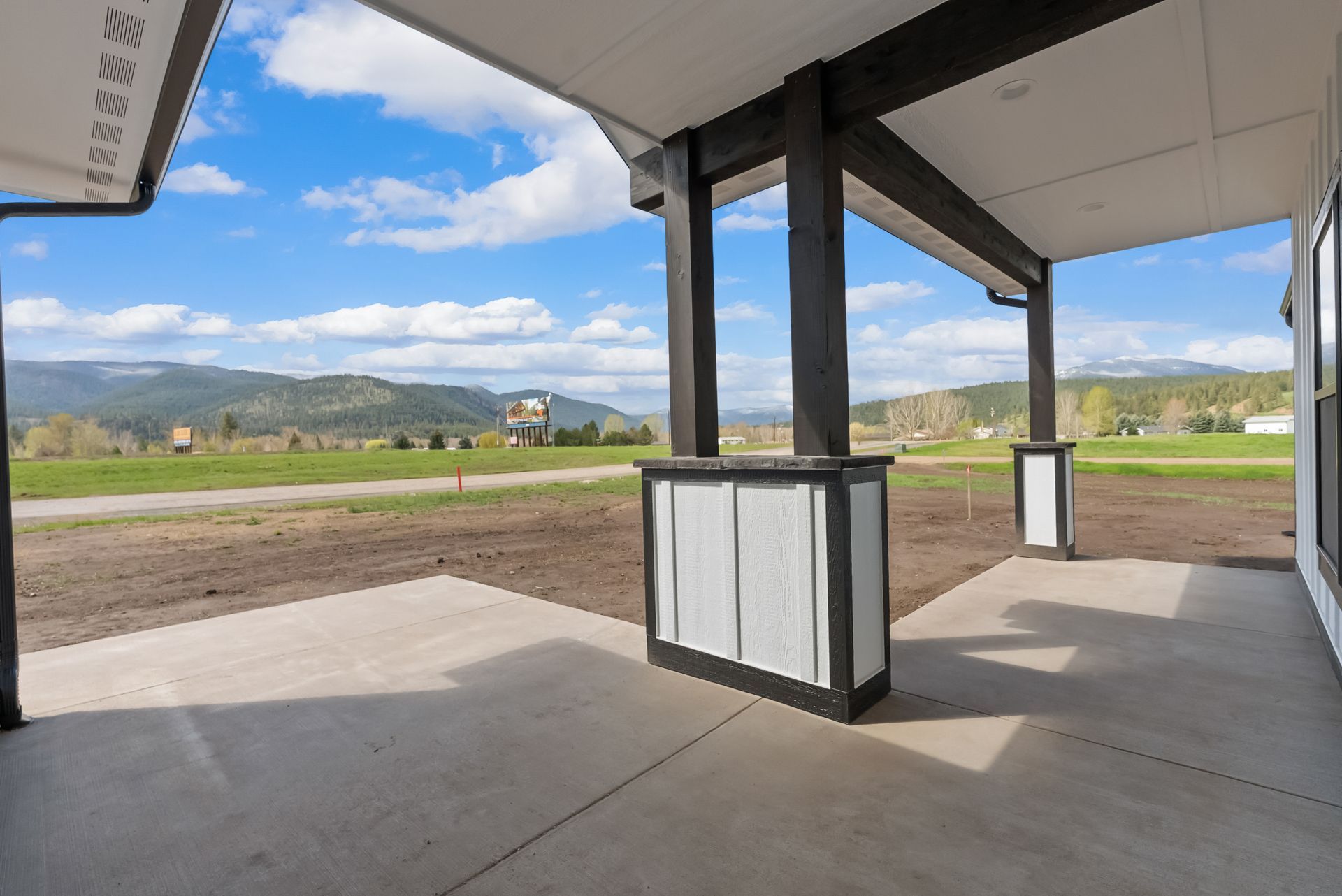 Covered patio with concrete floor, black posts, and open view of fields and mountains under a blue sky