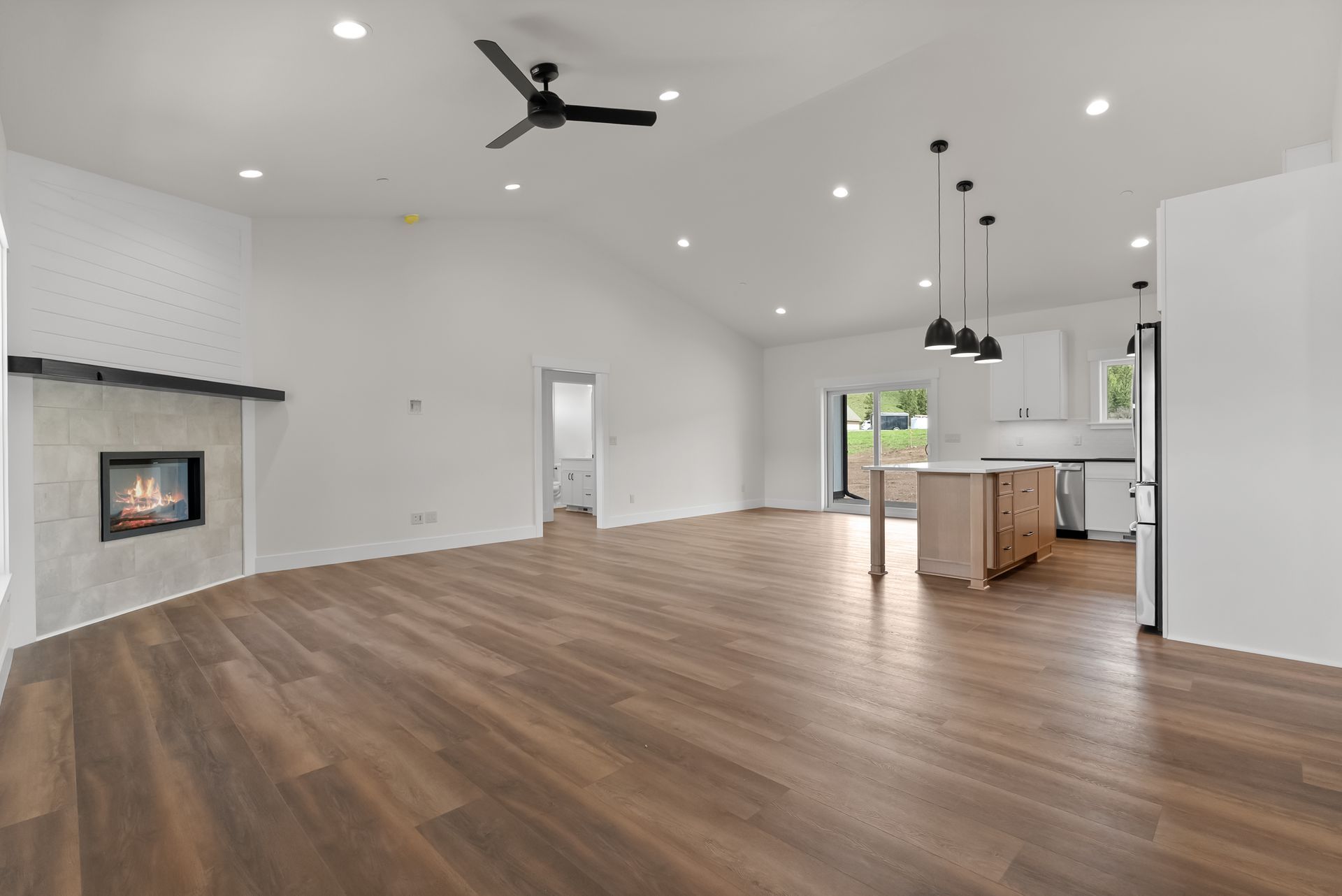 Open-concept living room with wood floors, white walls, ceiling fans, fireplace, and kitchen island
