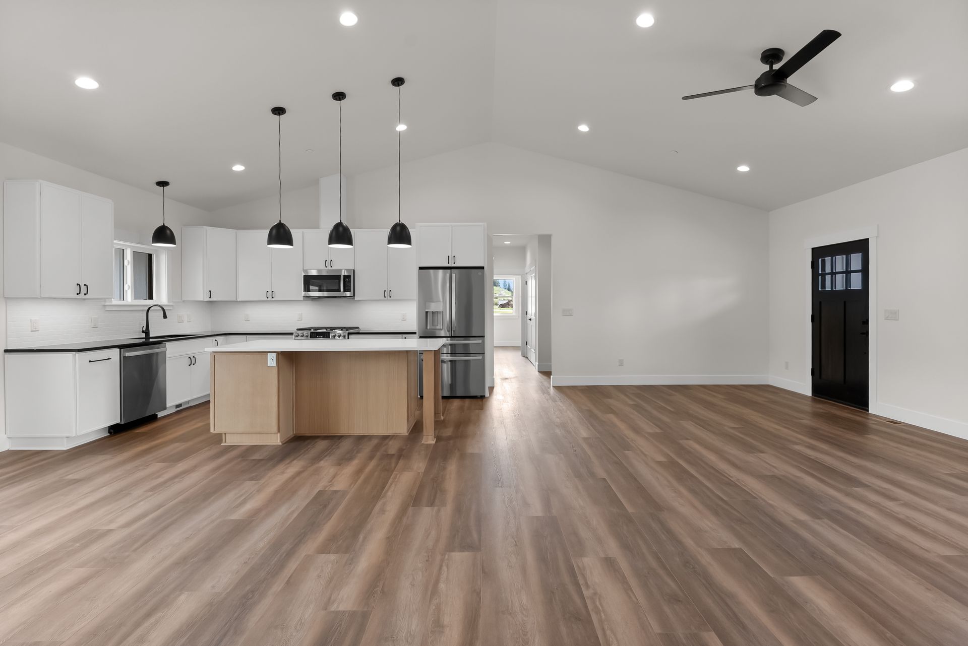 Spacious modern kitchen and living area with white walls, wood floors, island, and pendant lights