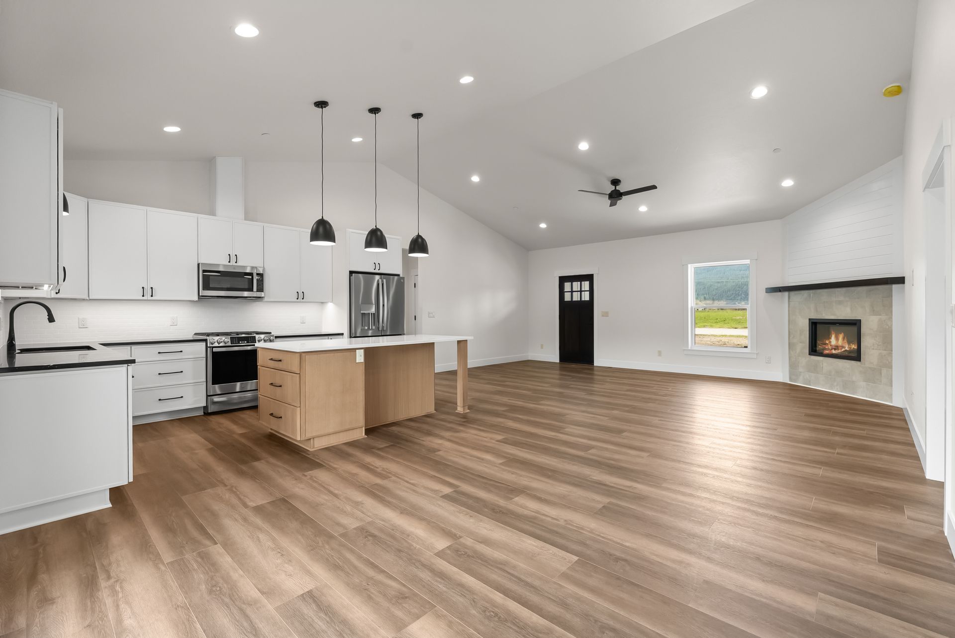 Open-plan kitchen and living room with white cabinets, wood floors, island, fireplace, and ceiling lights