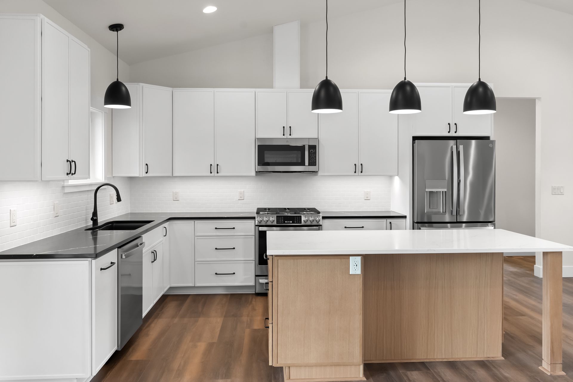 Modern white kitchen with black pendant lights, stainless appliances, and a wood-topped island.
