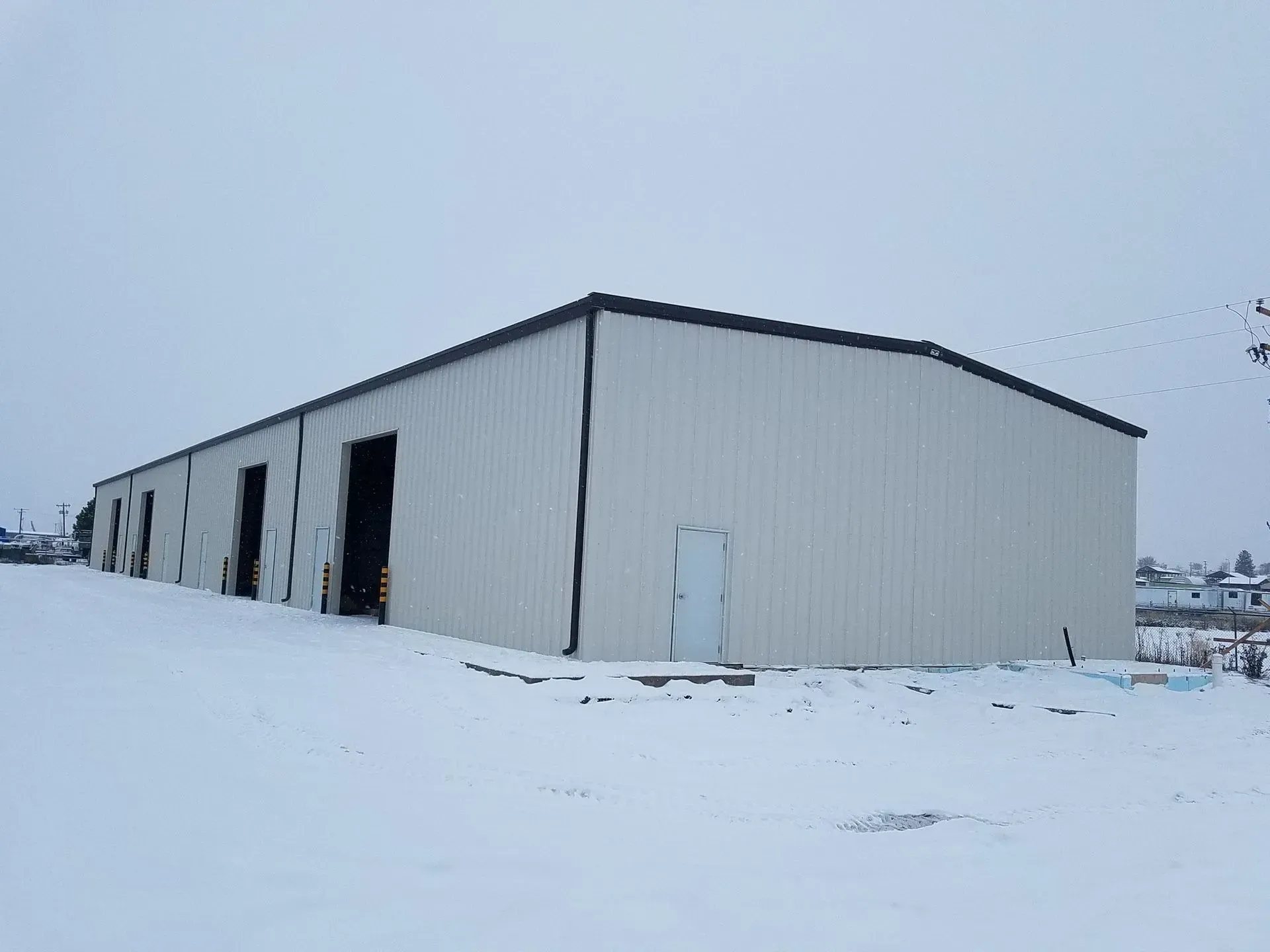 Snow-covered industrial warehouse with beige metal siding under a gray winter sky