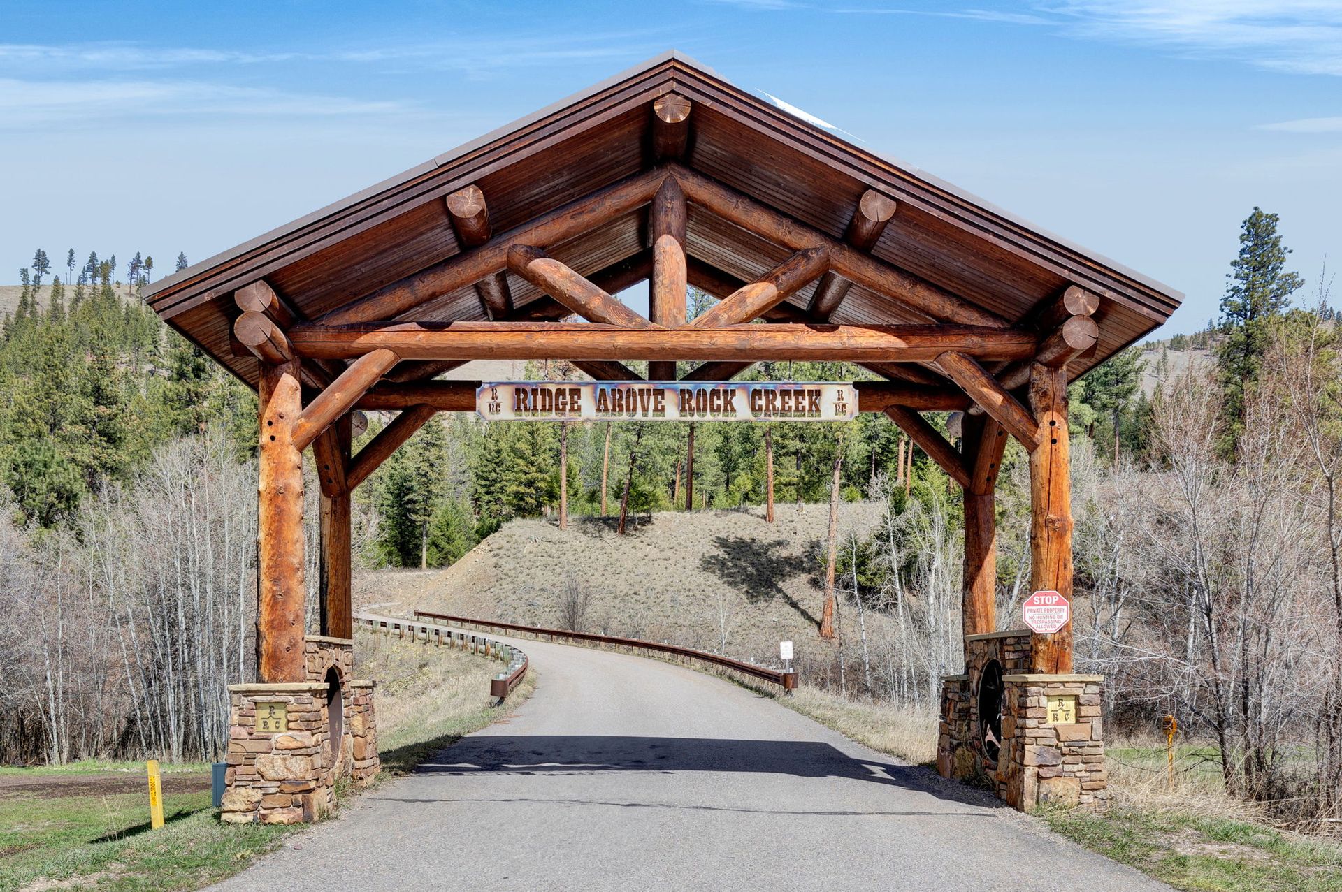 Wooden log archway over a paved road in a wooded area