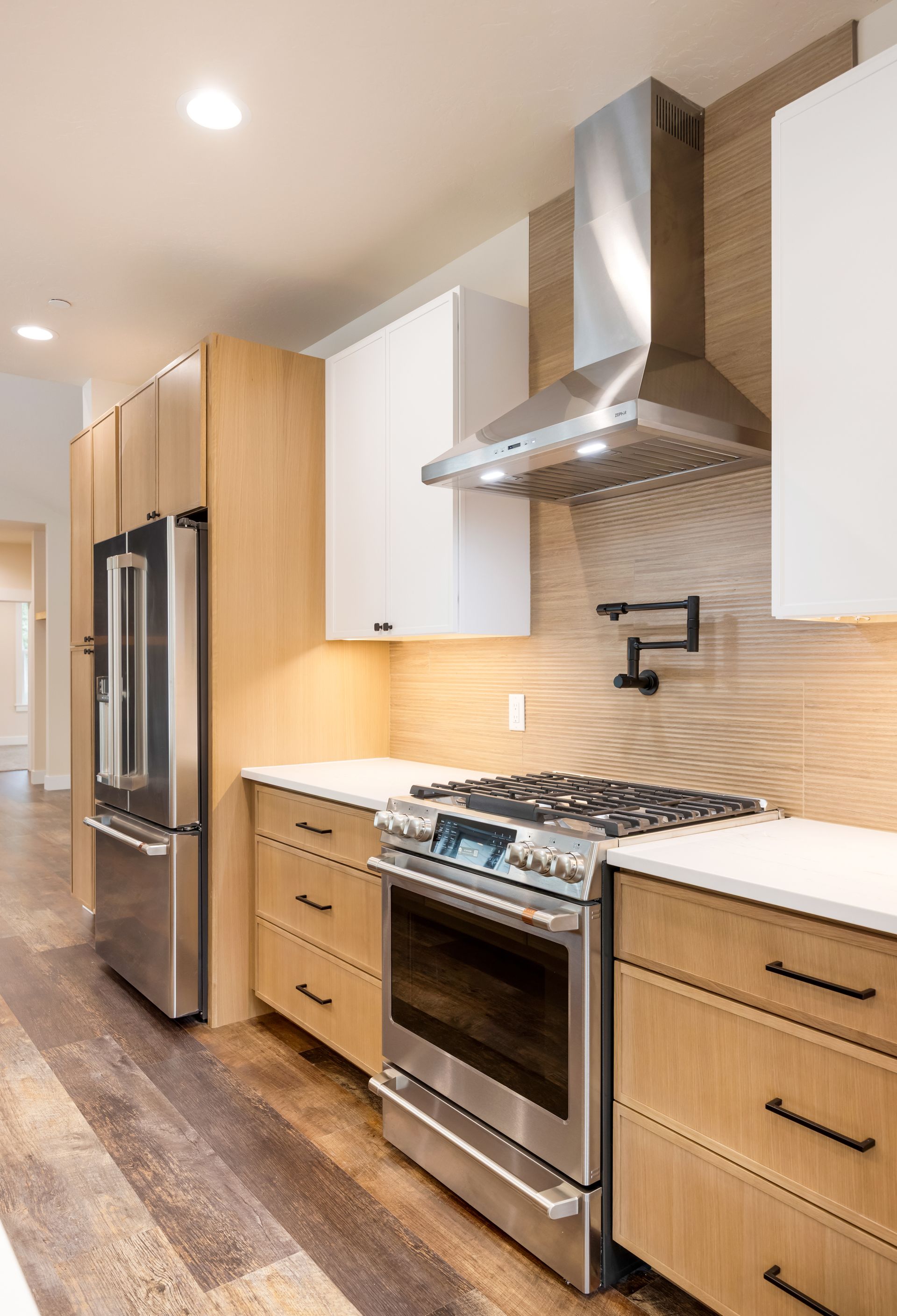 Modern kitchen with stainless steel appliances, wood cabinets, white counters, and tiled backsplash