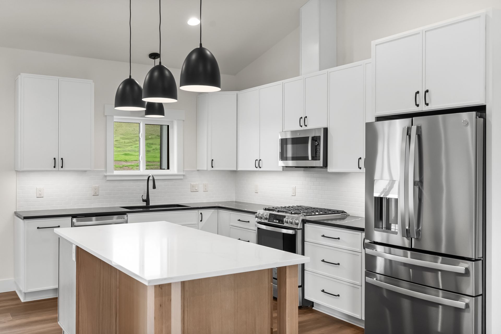 Bright modern kitchen with white cabinets, stainless steel appliances, island, and black pendant lights