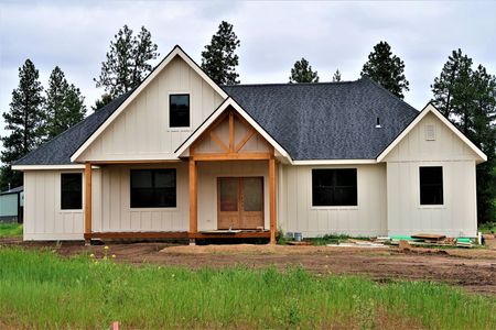 New beige house under construction with dark roof and front porch on a grassy lot