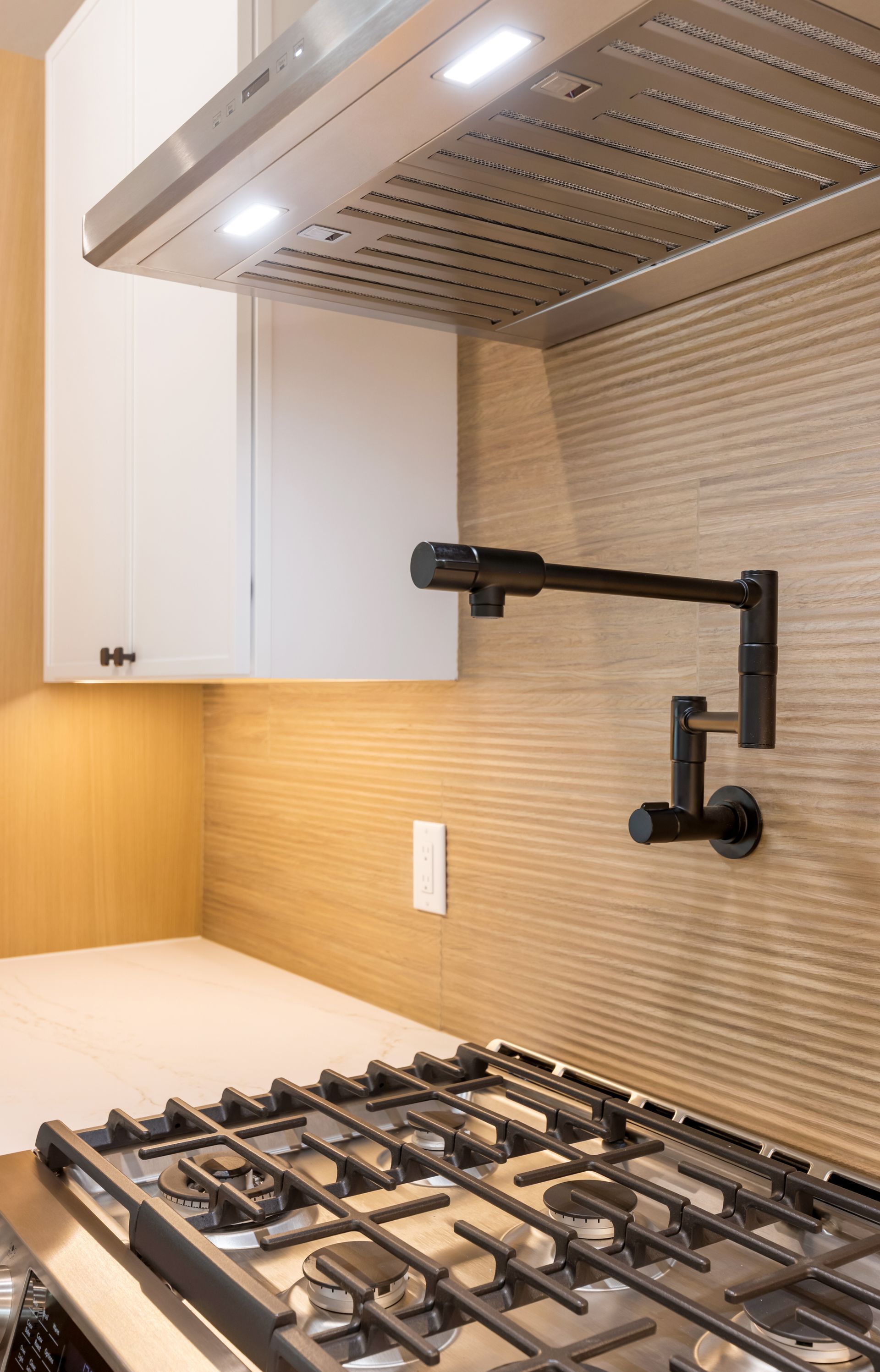 Modern kitchen with gas cooktop, white cabinets, tiled backsplash, and wall-mounted faucet under a vent hood