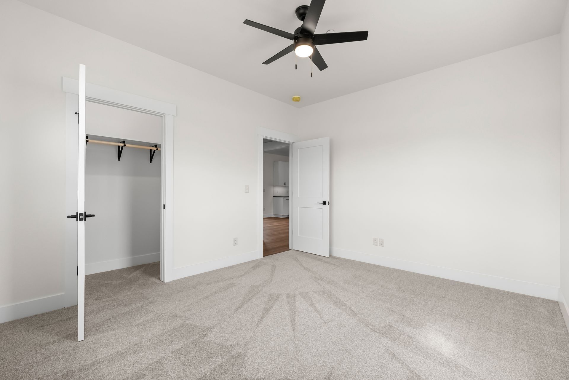 Empty white bedroom with gray carpet, open closet door, and ceiling fan