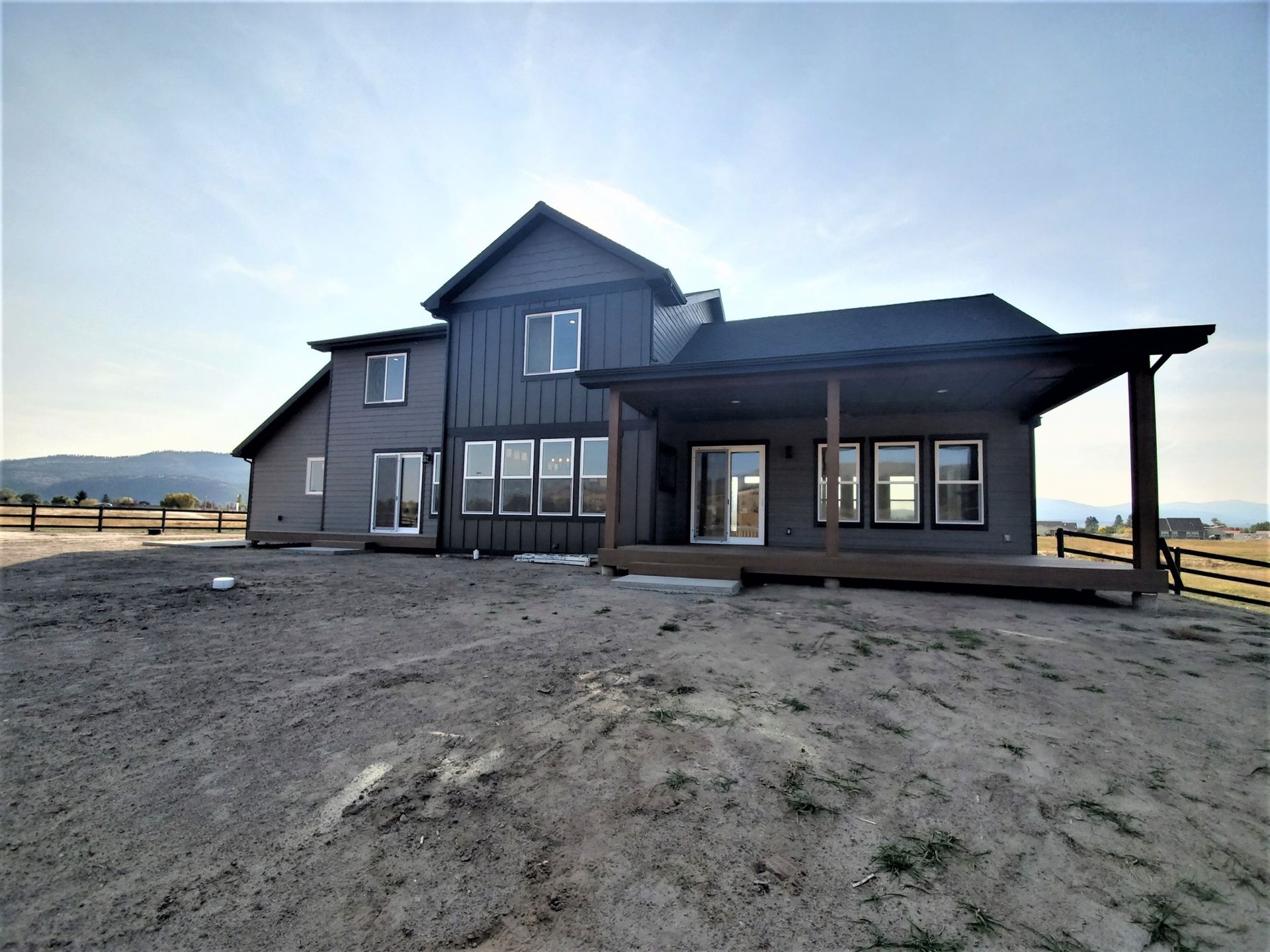 Modern gray farmhouse with covered porch on a dirt lot at sunset