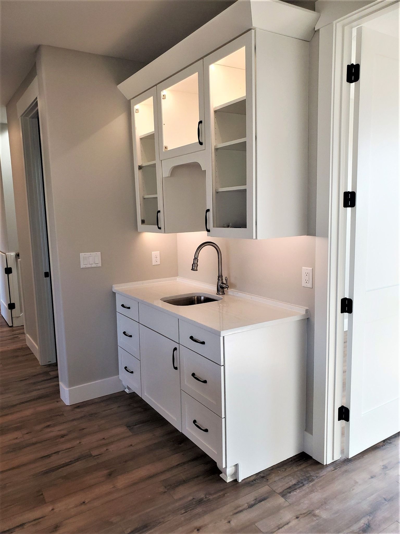 White bathroom vanity with double sinks, mirrors, and a partially open cabinet in a hallway.