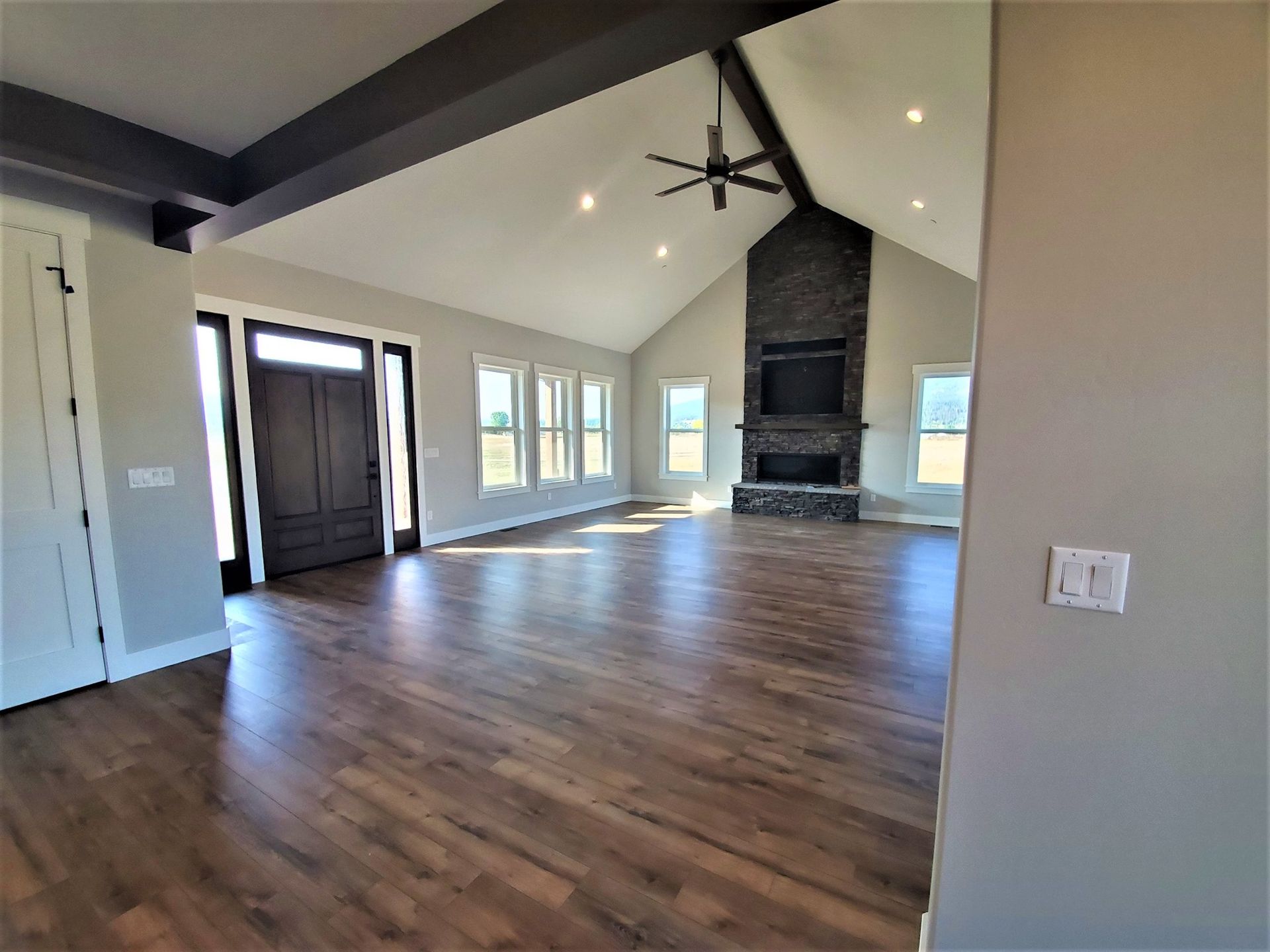 Spacious empty living room with vaulted ceiling, dark wood floors, fireplace, and large windows