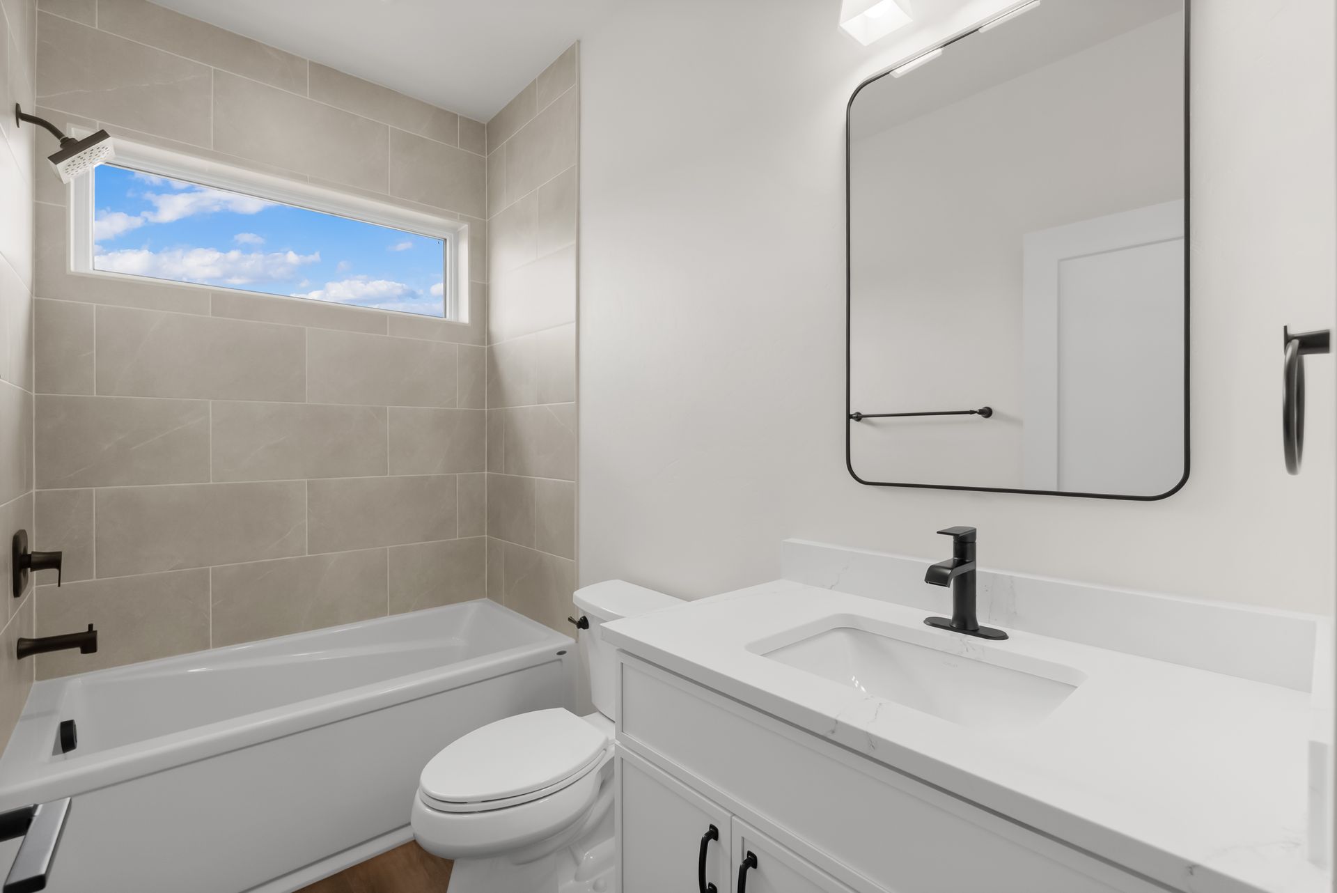 Bright white bathroom with bathtub, vanity sink, mirror, and small window with sky view