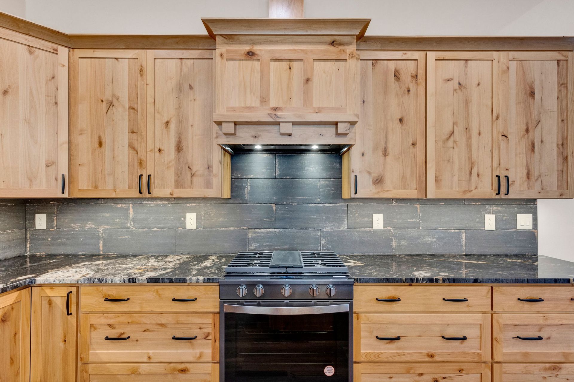 Wooden kitchen cabinets with granite countertops and a stainless steel stove and backsplash
