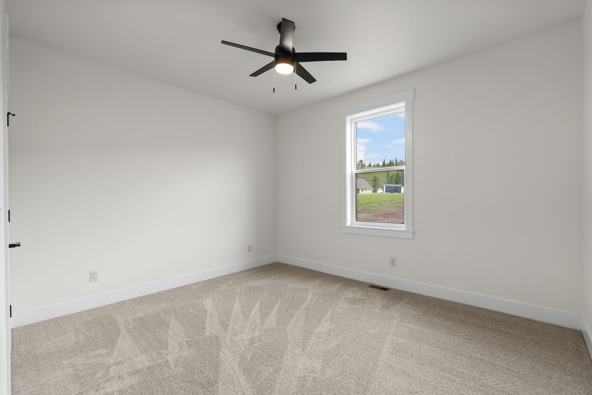 Empty carpeted bedroom with white walls, ceiling fan, and a single window.