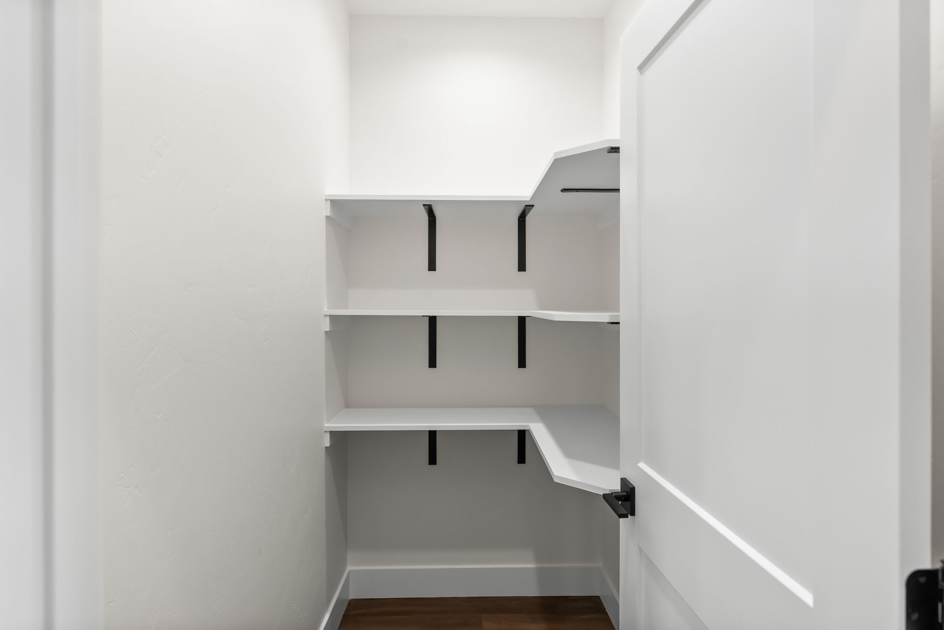 Empty white walk-in pantry with built-in shelves and wood floor.