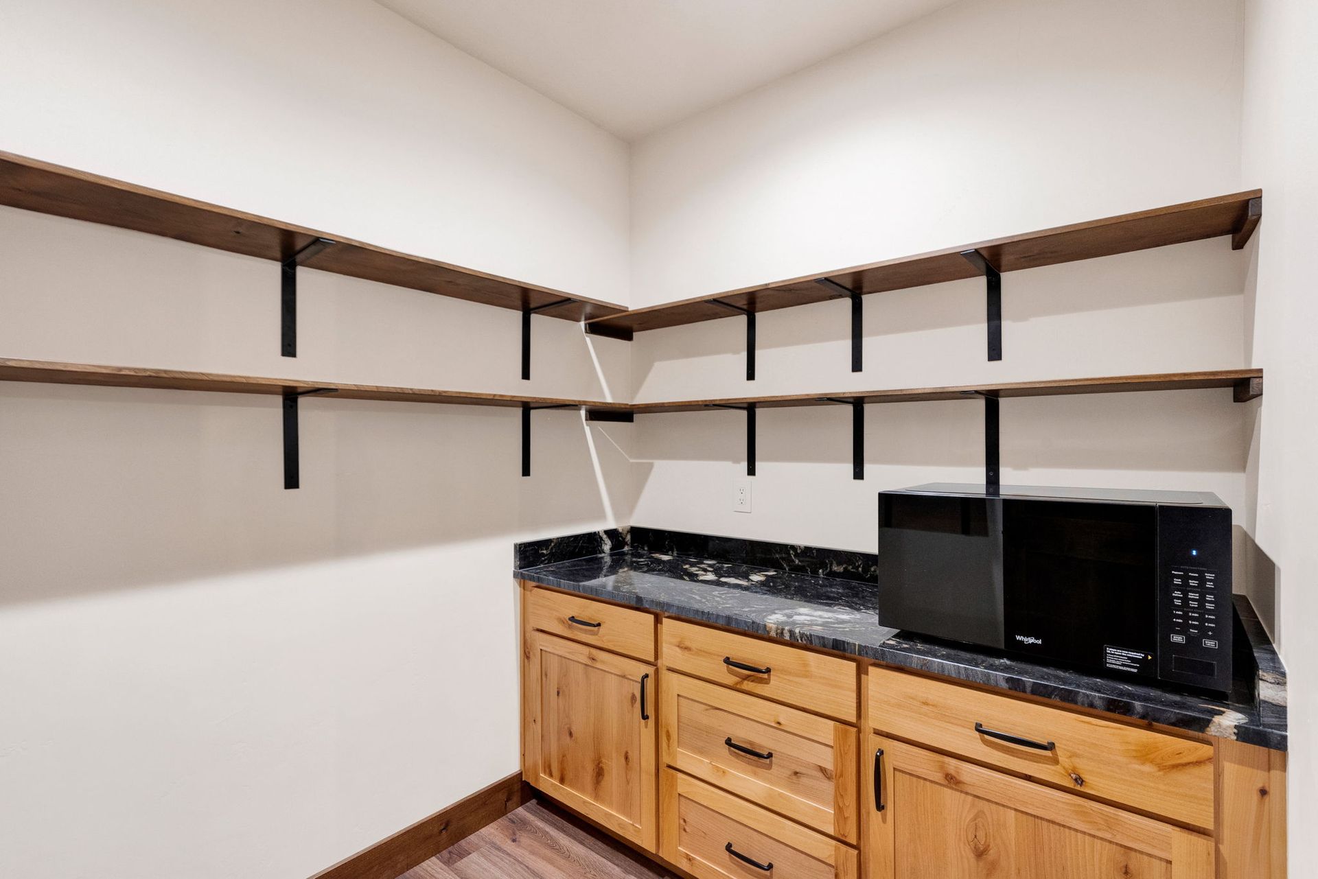 Empty kitchen corner with wooden cabinets, black countertop, and dark wall shelves.