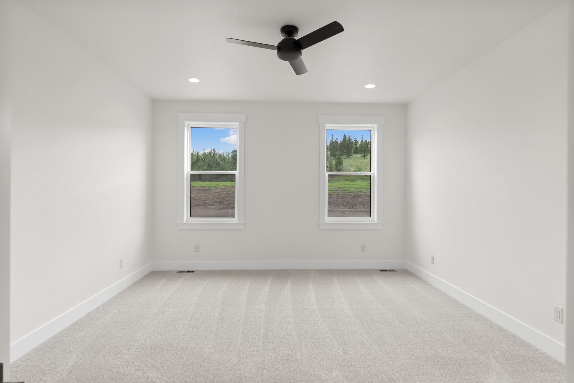 Empty white bedroom with two windows, gray carpet, and a black ceiling fan