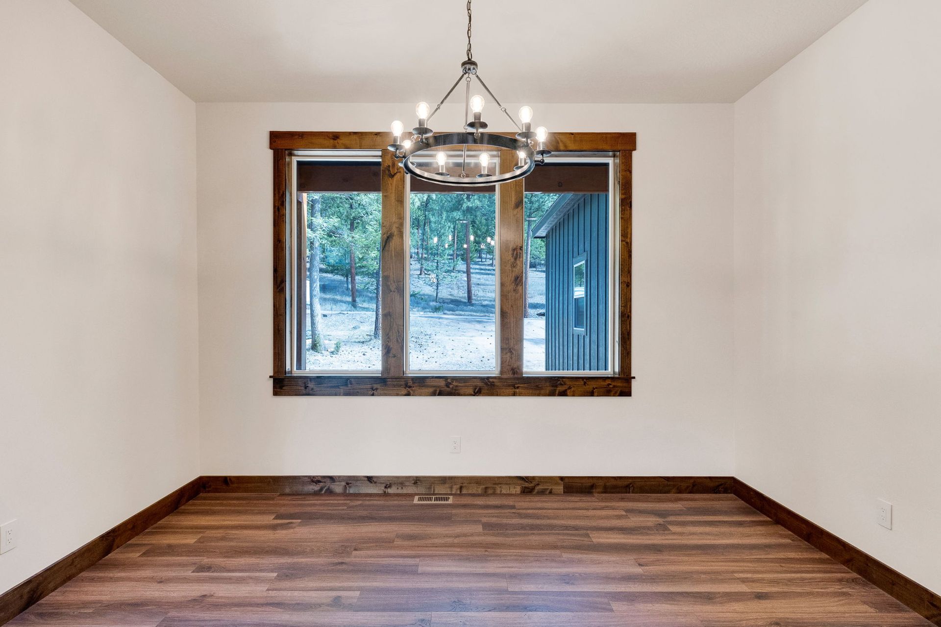 Empty dining room with hardwood floors, white walls, chandelier, and window overlooking snowy trees