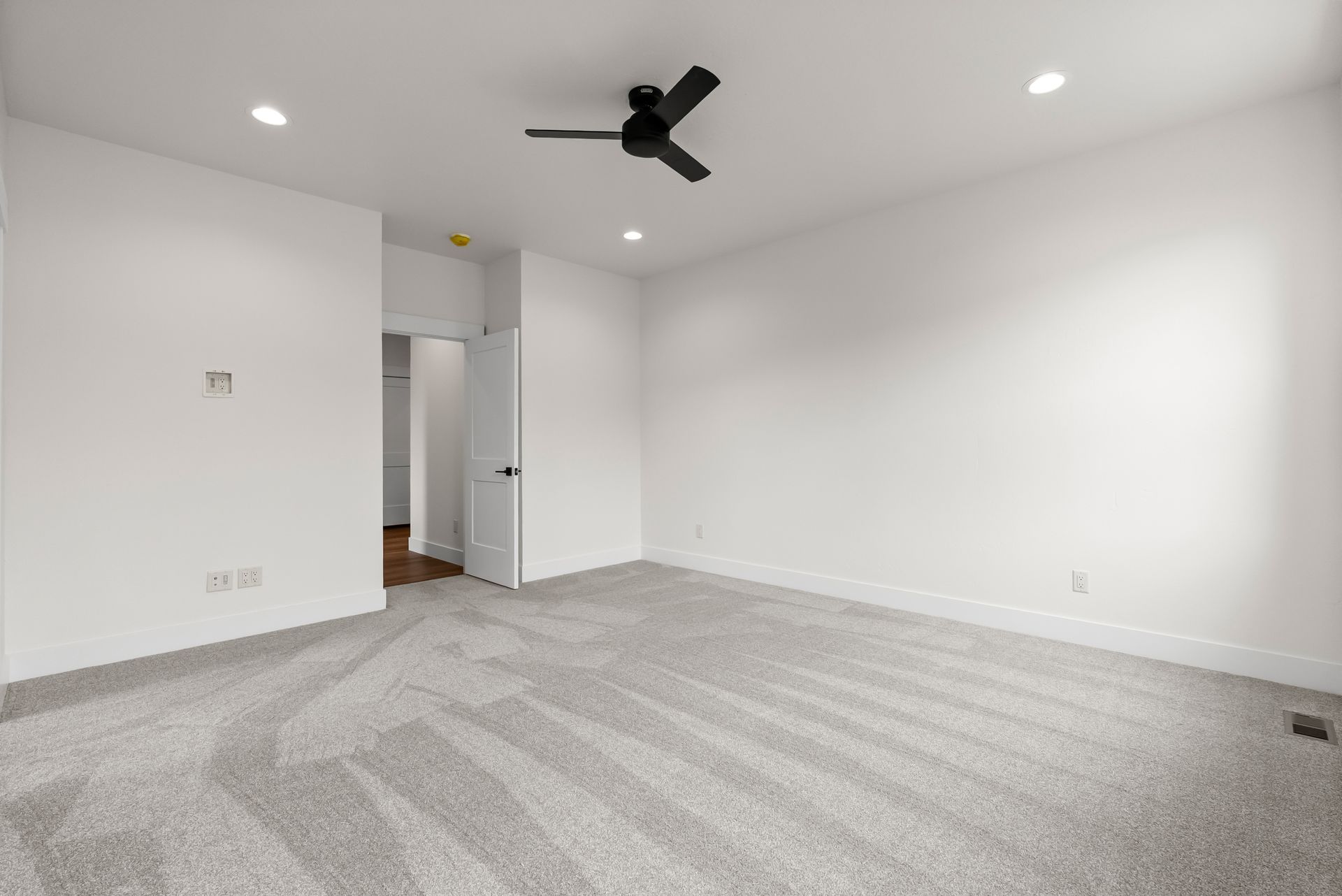 Empty white bedroom with gray carpet and a ceiling fan, viewed from the doorway