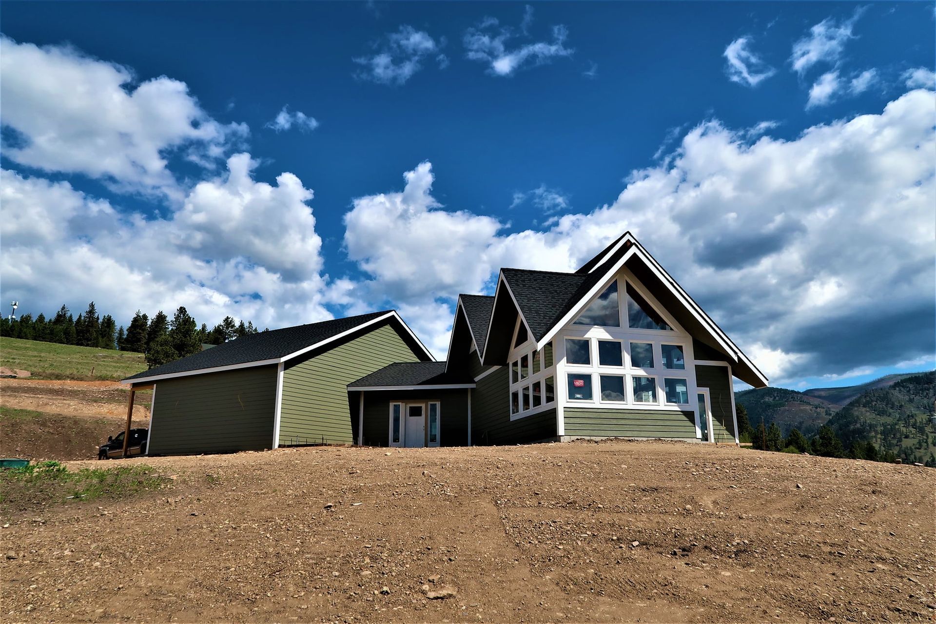 Modern mountain house with green siding under a bright blue sky and clouds