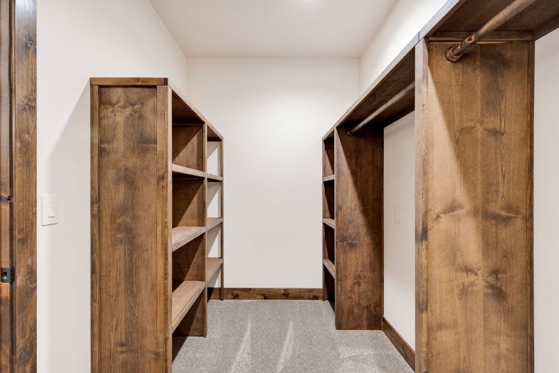 Empty walk-in closet with wooden shelves and hanging rods on both sides, carpeted floor, and white walls