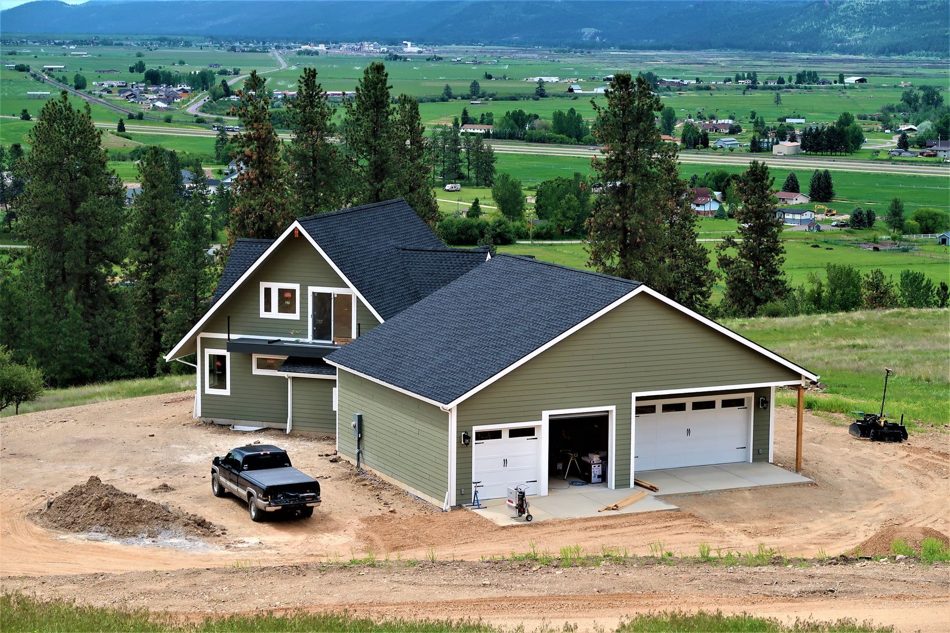 New suburban house with dark roof, parked car, and green fields in the background