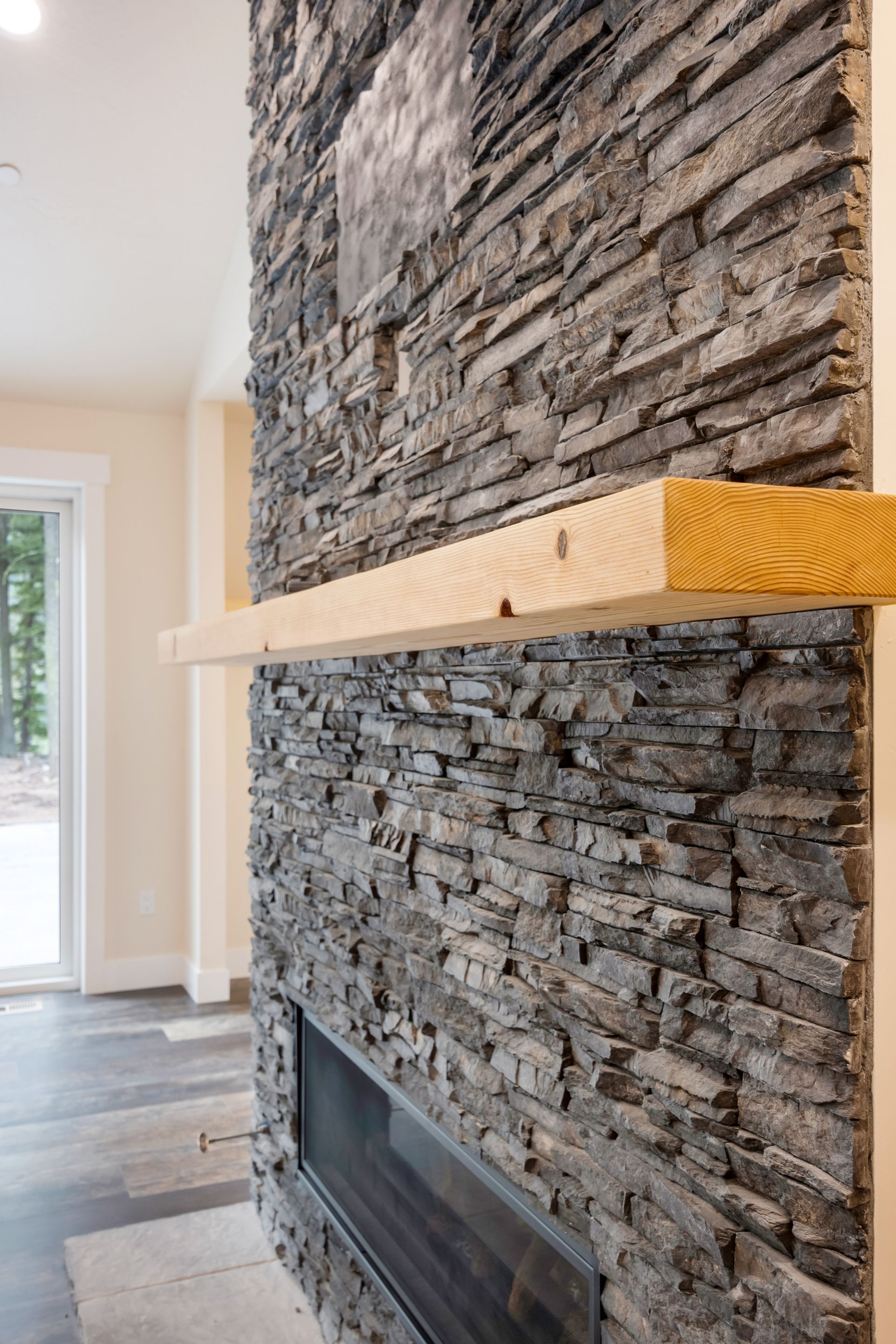 Stacked stone fireplace with a wooden mantel in a bright modern living room
