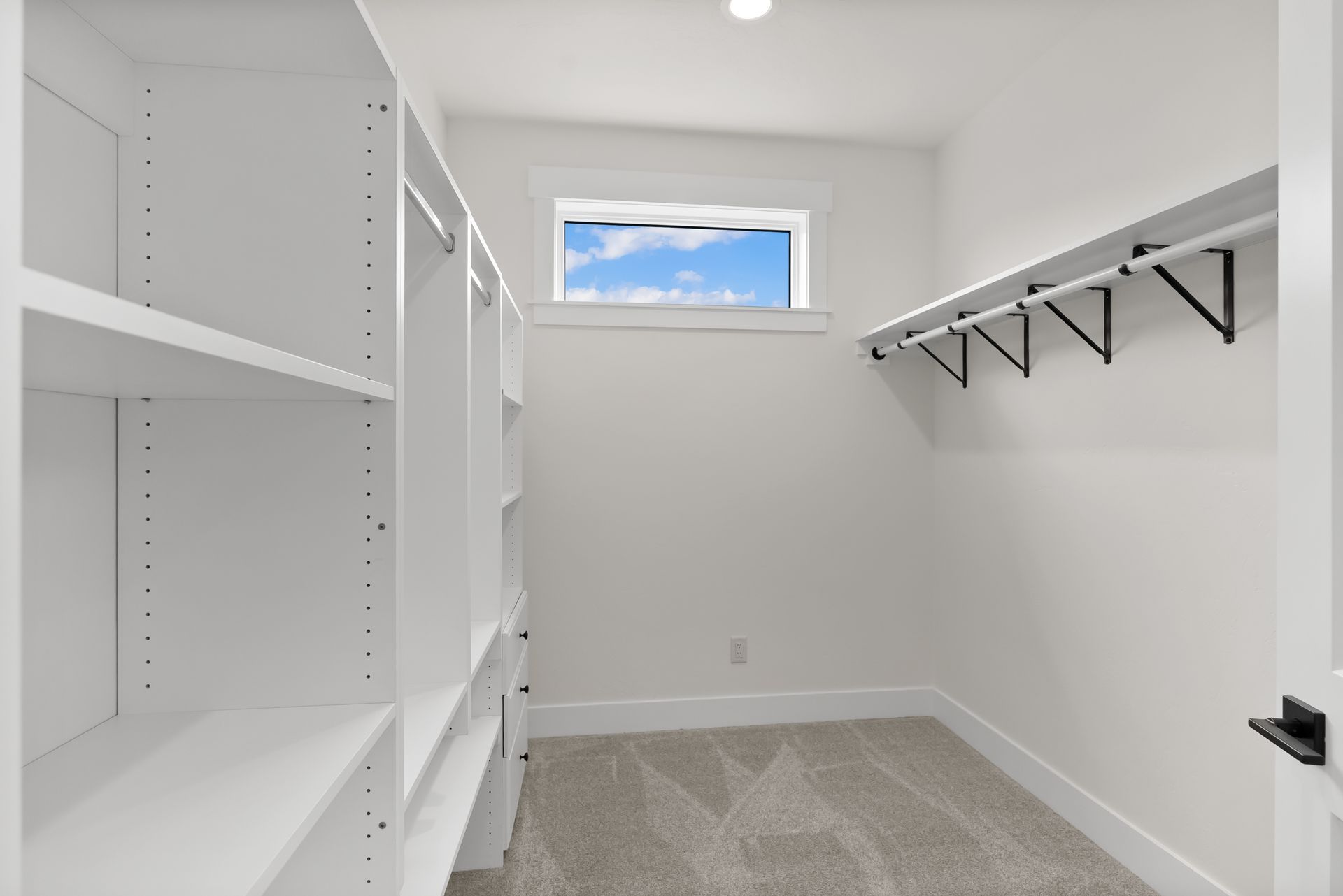 Bright white walk-in closet with built-in shelves, hanging rods, and a small window.