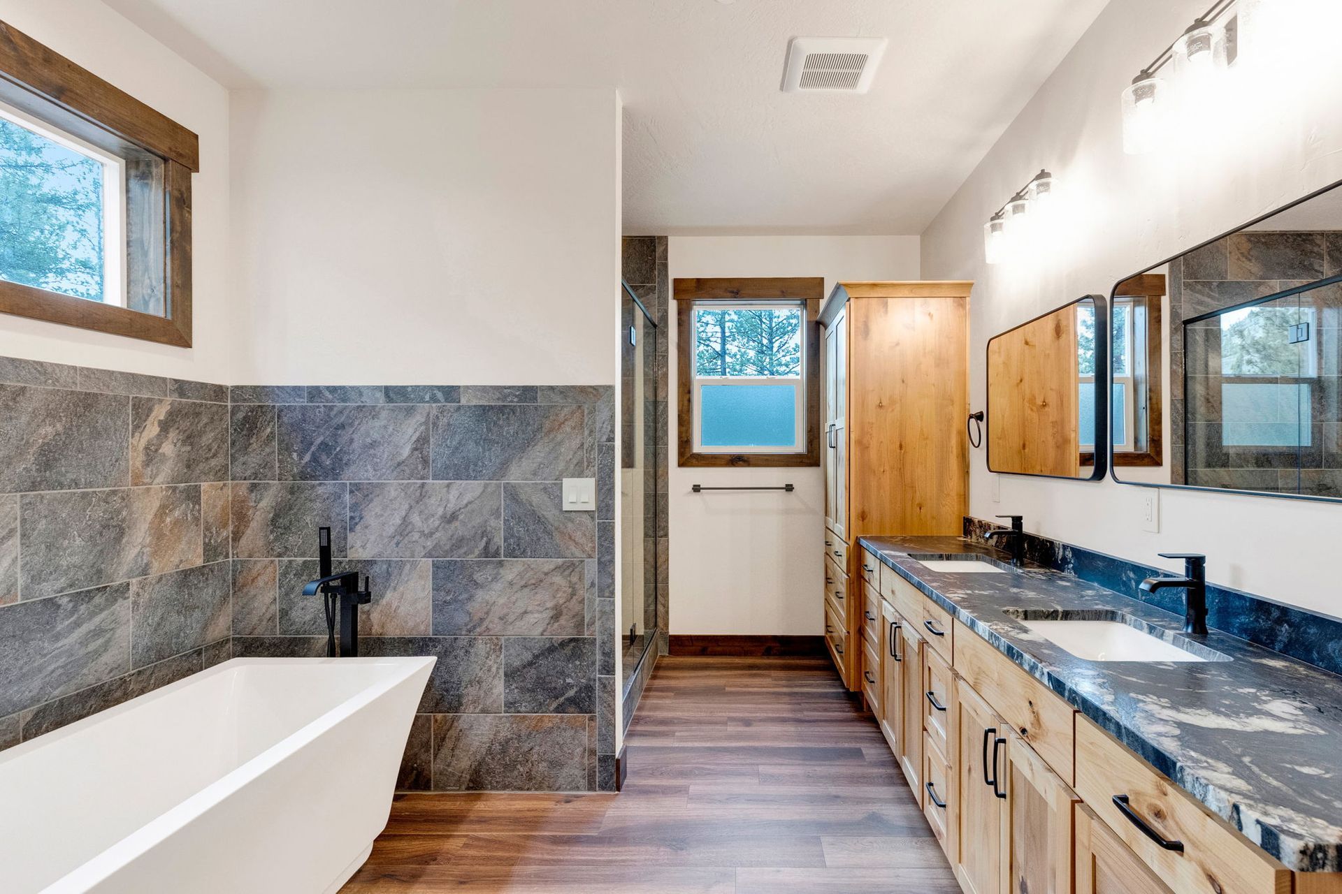 Modern bathroom with a bathtub, double vanity, wood floors, and large mirror.