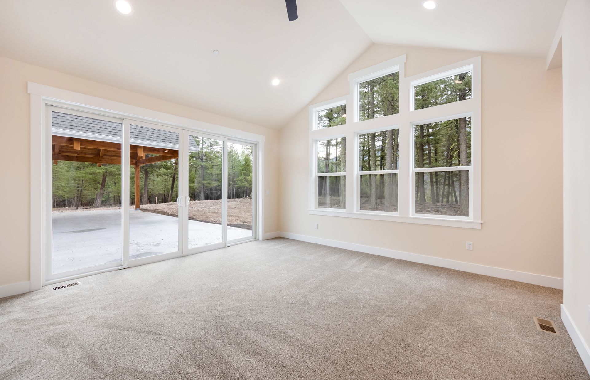 Bright empty living room with carpet, large windows, and sliding glass doors to a patio.