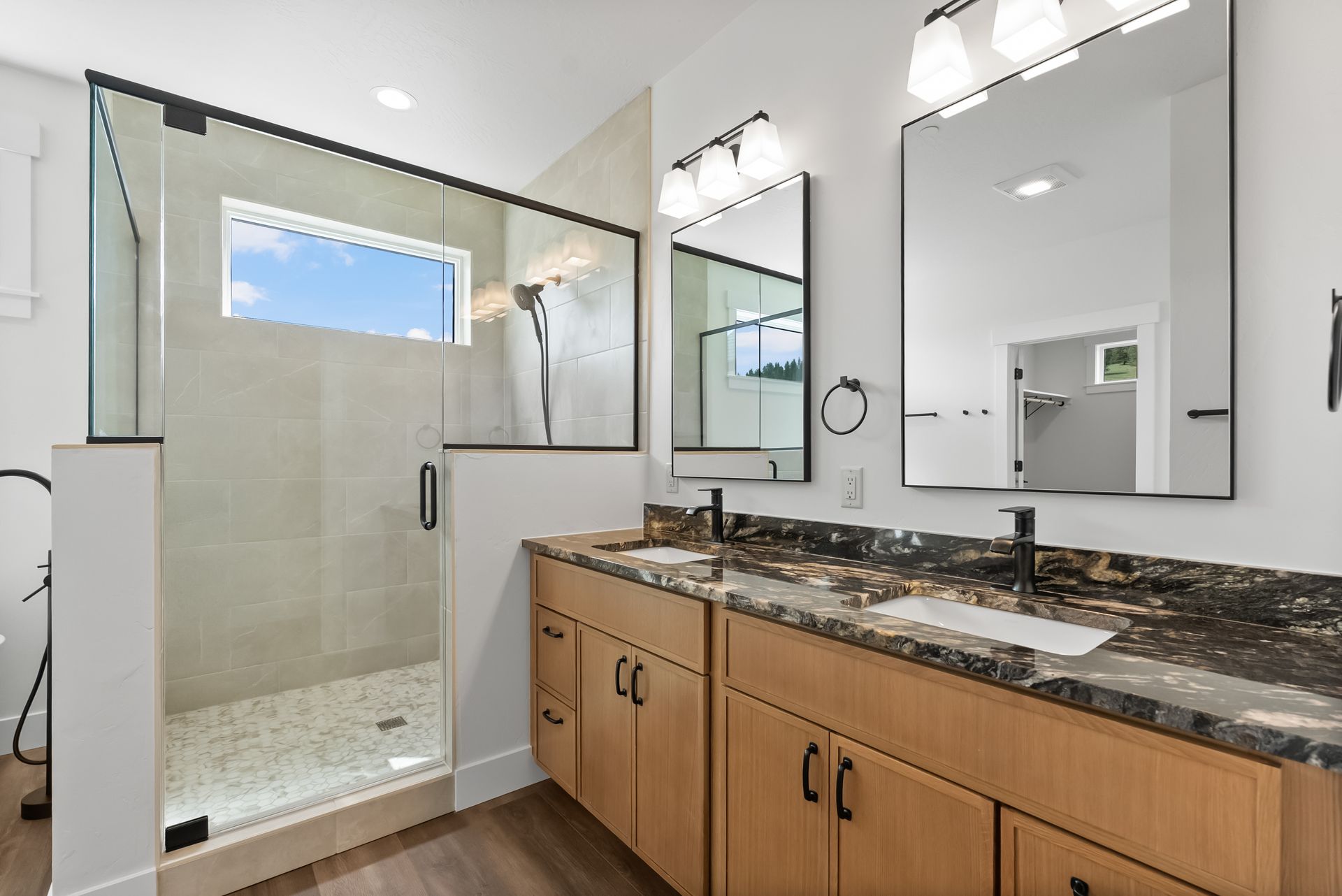 Modern bathroom with glass shower, wood vanity, granite countertop, and large mirror with bright white walls