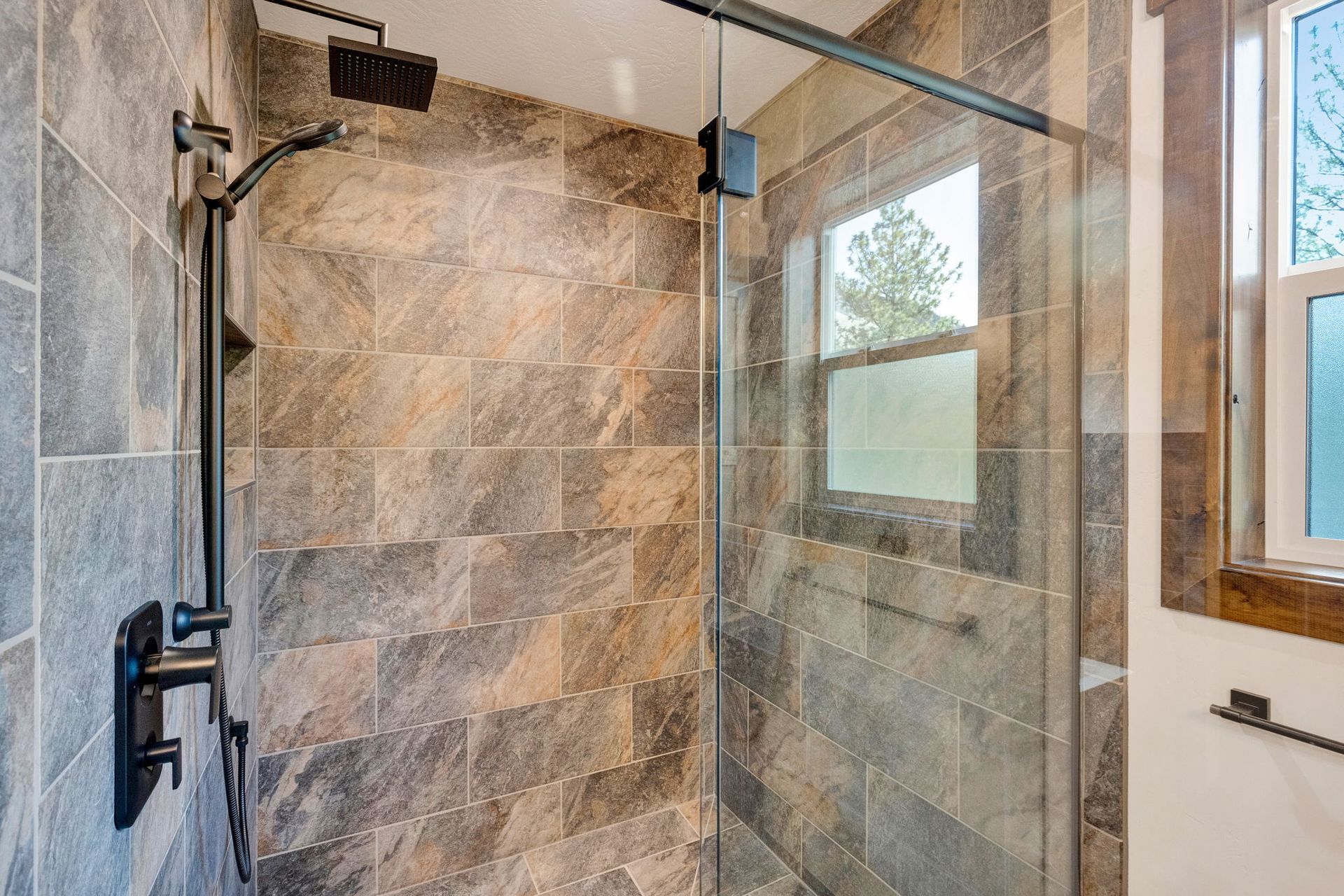 Glass shower enclosure with stone-tiled walls and black fixtures in a bathroom
