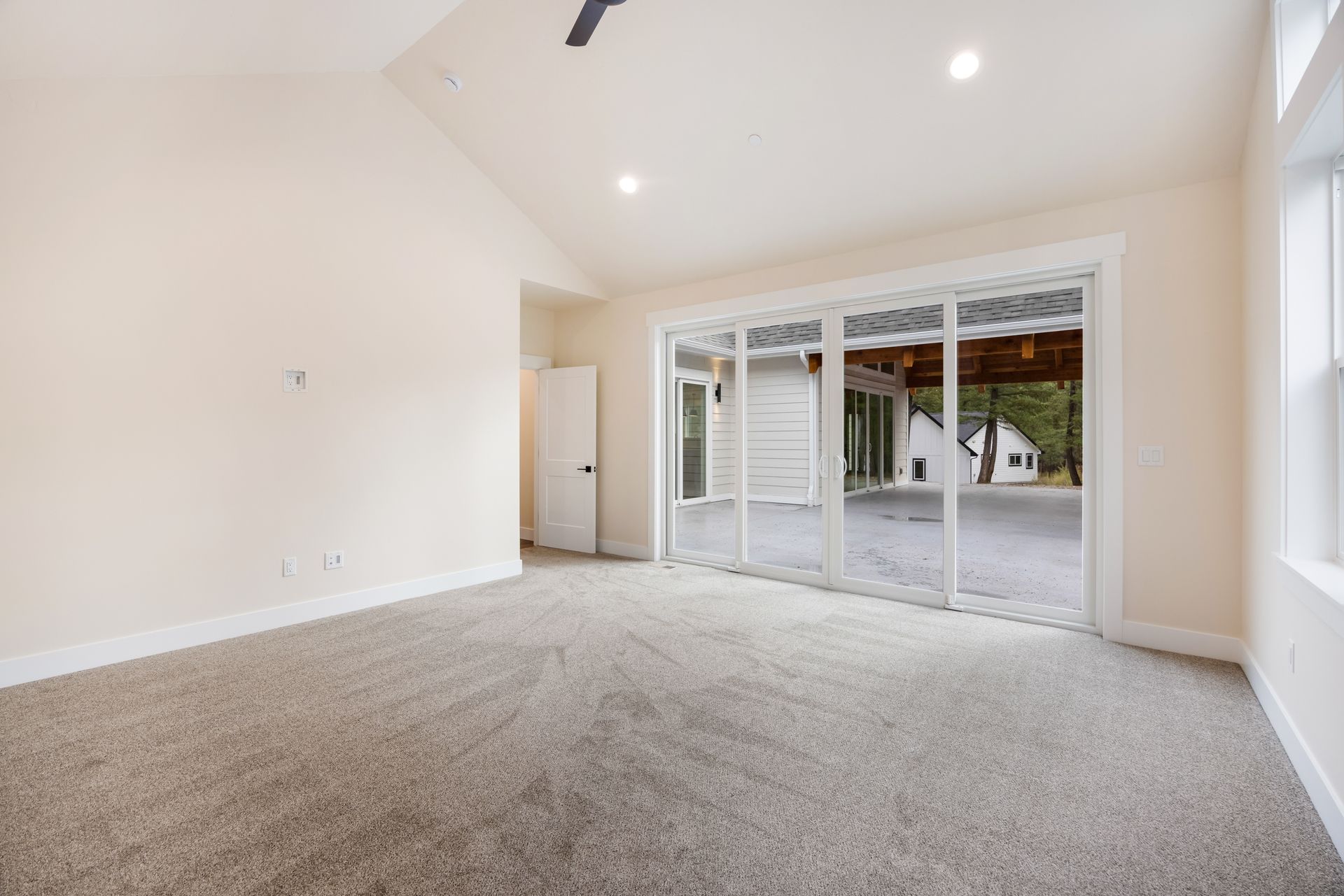 Bright empty living room with carpet, vaulted ceiling, and sliding glass doors to a patio.