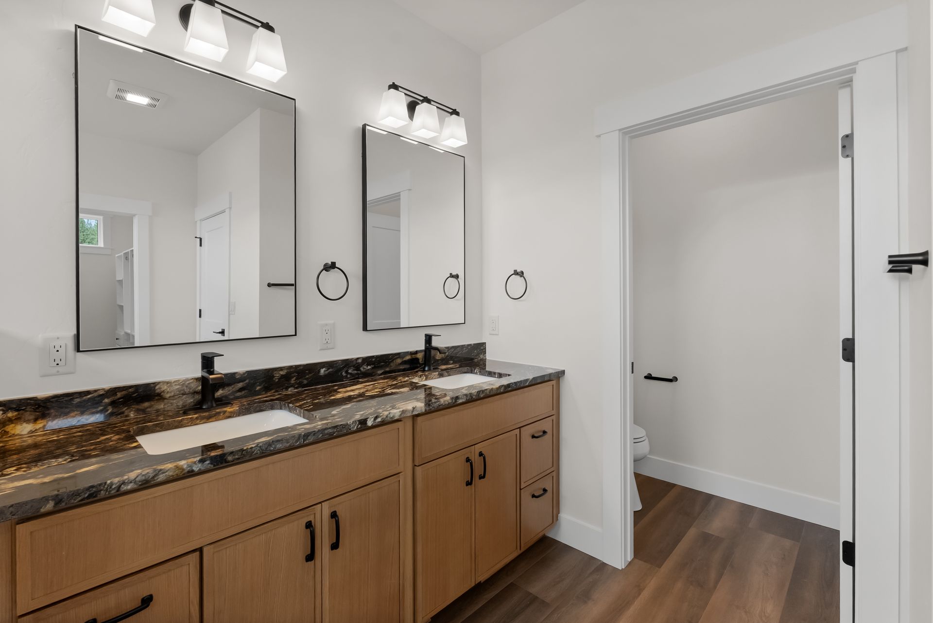 Modern bathroom with double vanity, mirrors, wood cabinets, and open doorway to a hallway