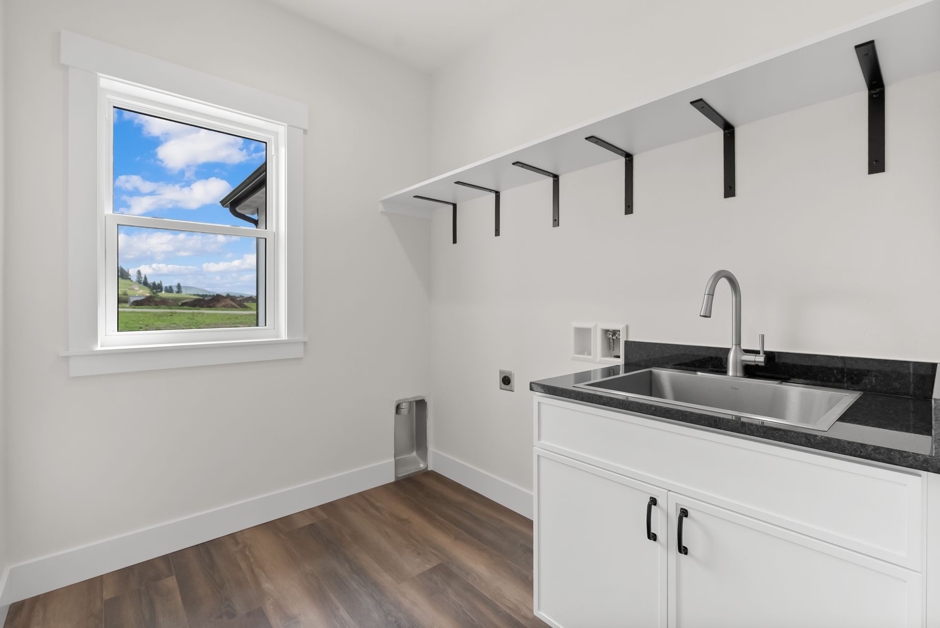 Bright white laundry room with sink, shelf, and window overlooking a grassy landscape