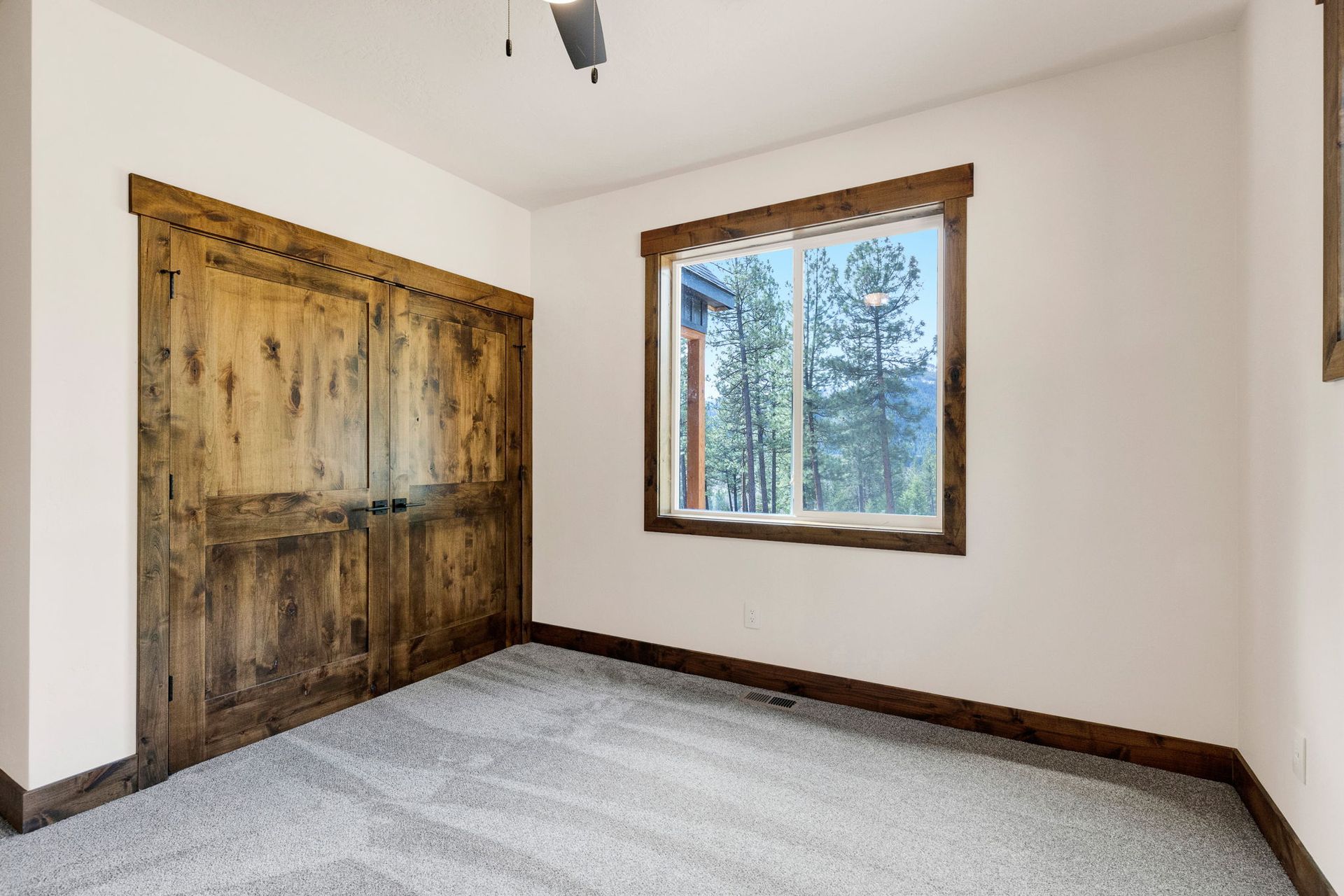 Empty bedroom with rustic barn-style closet doors and a window showing trees outside