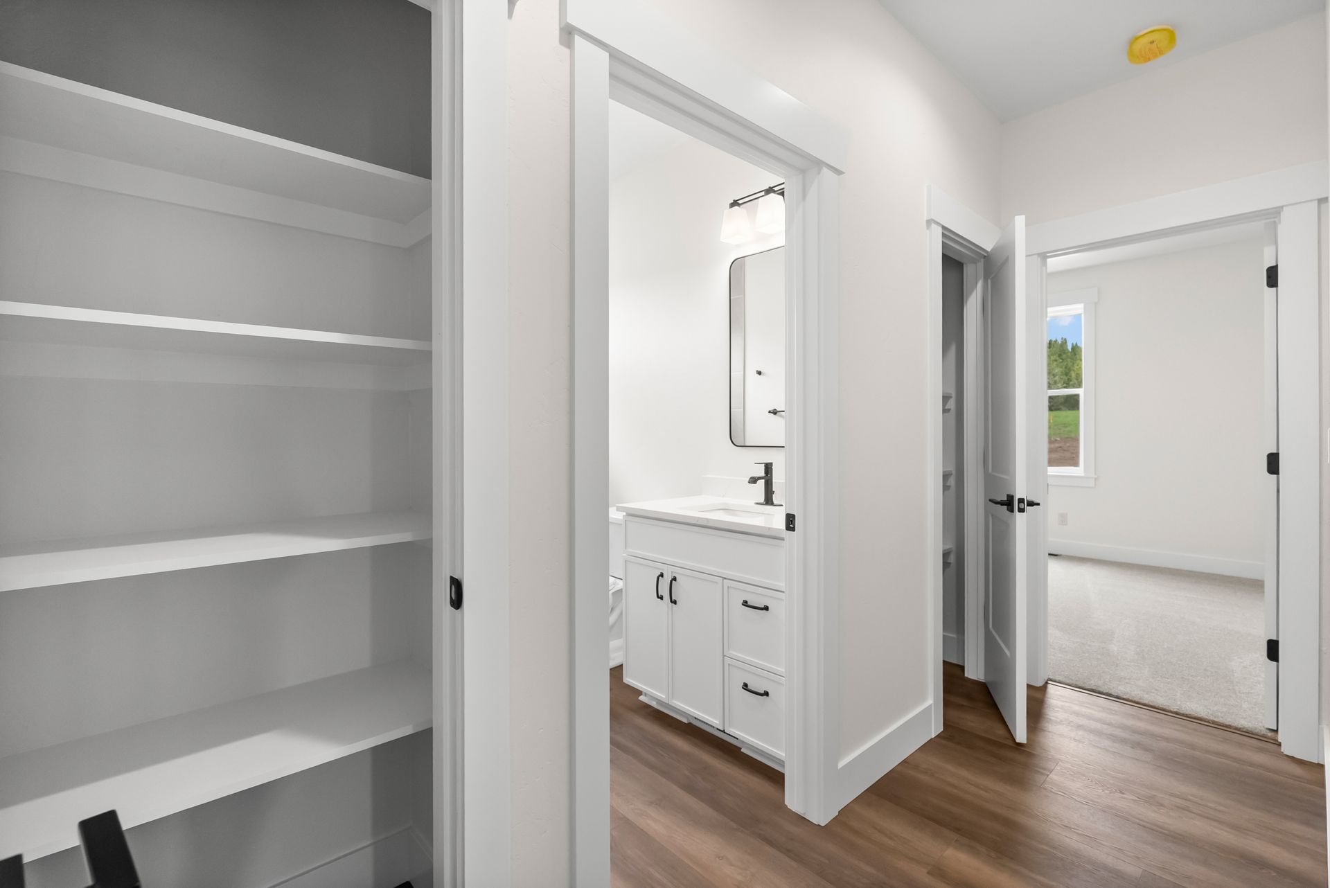 Bright hallway with white walls, open closets, and a bathroom vanity visible through an open door.
