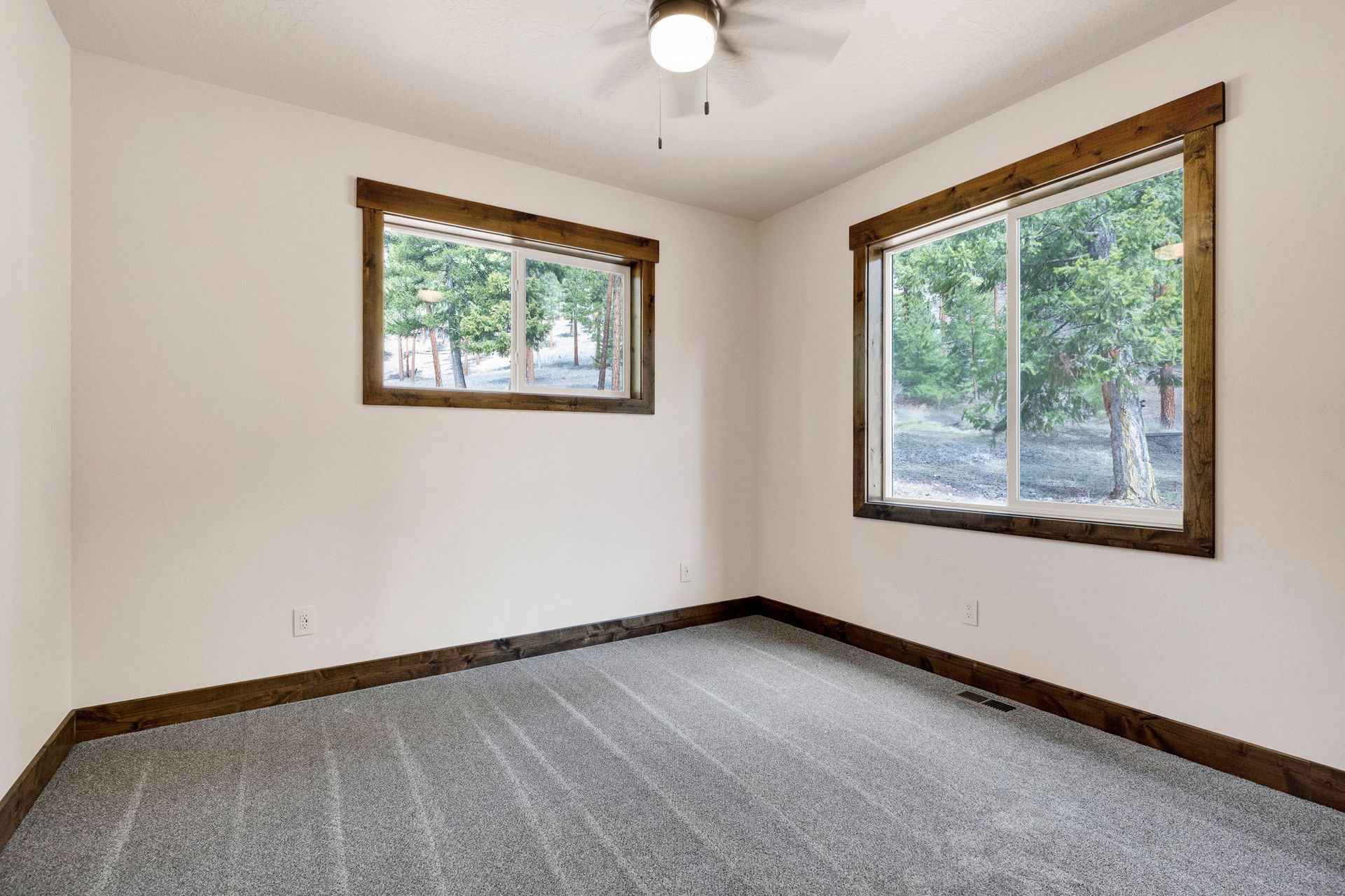 Empty carpeted room with white walls, wood trim, and two windows letting in daylight