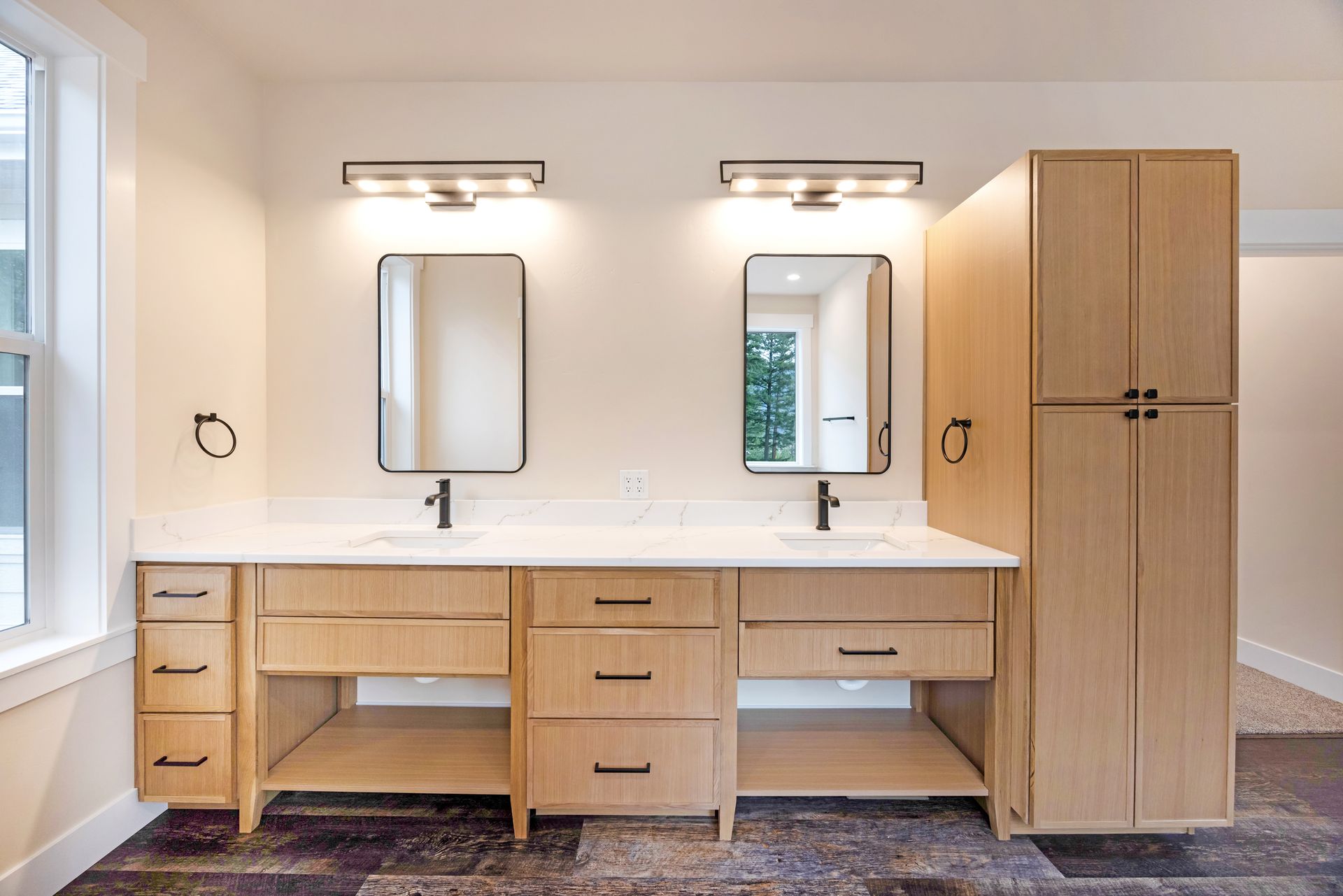 Modern bathroom vanity with double sinks, mirrors, lights, drawers, and a tall wood cabinet