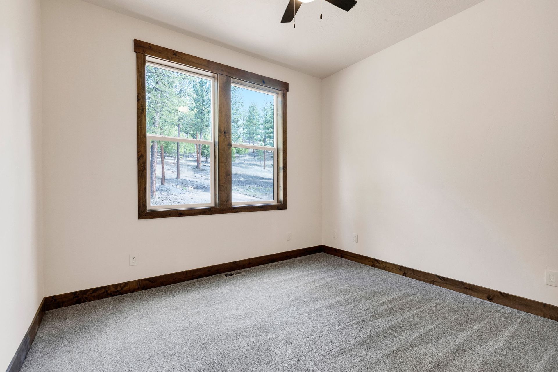 Empty carpeted bedroom with white walls and a window looking out to trees and snow