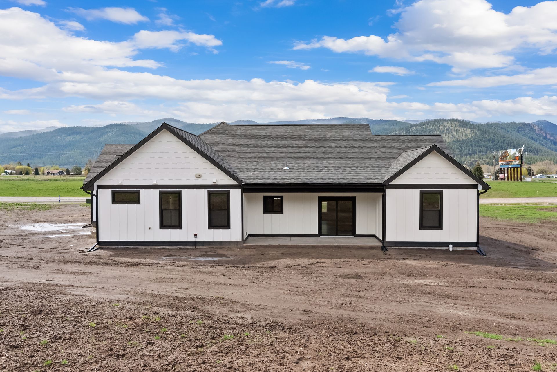 New white single-story house with dark roof on a muddy lot under a blue sky