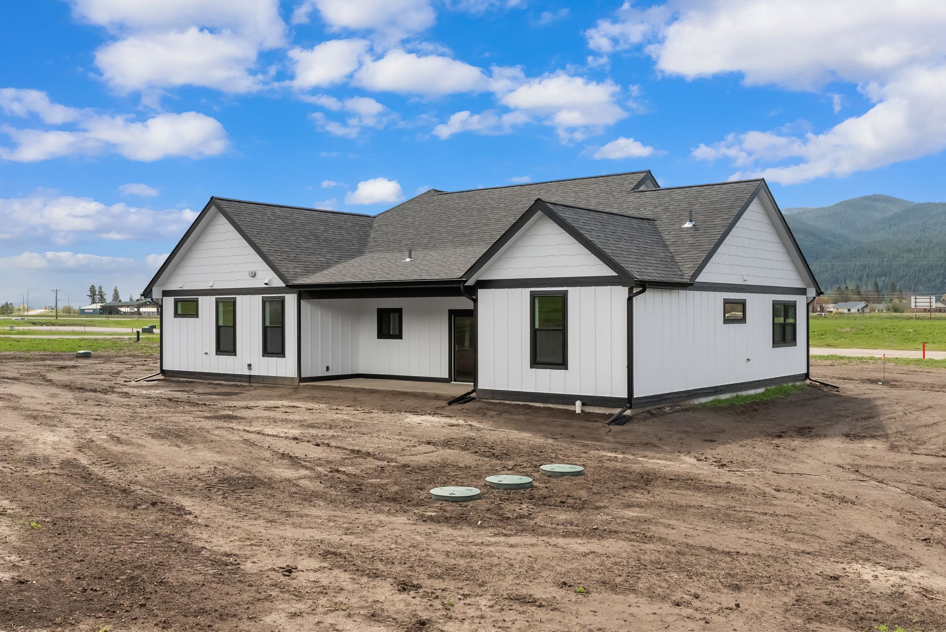 New white house with gray roof under a blue sky on a dirt lot