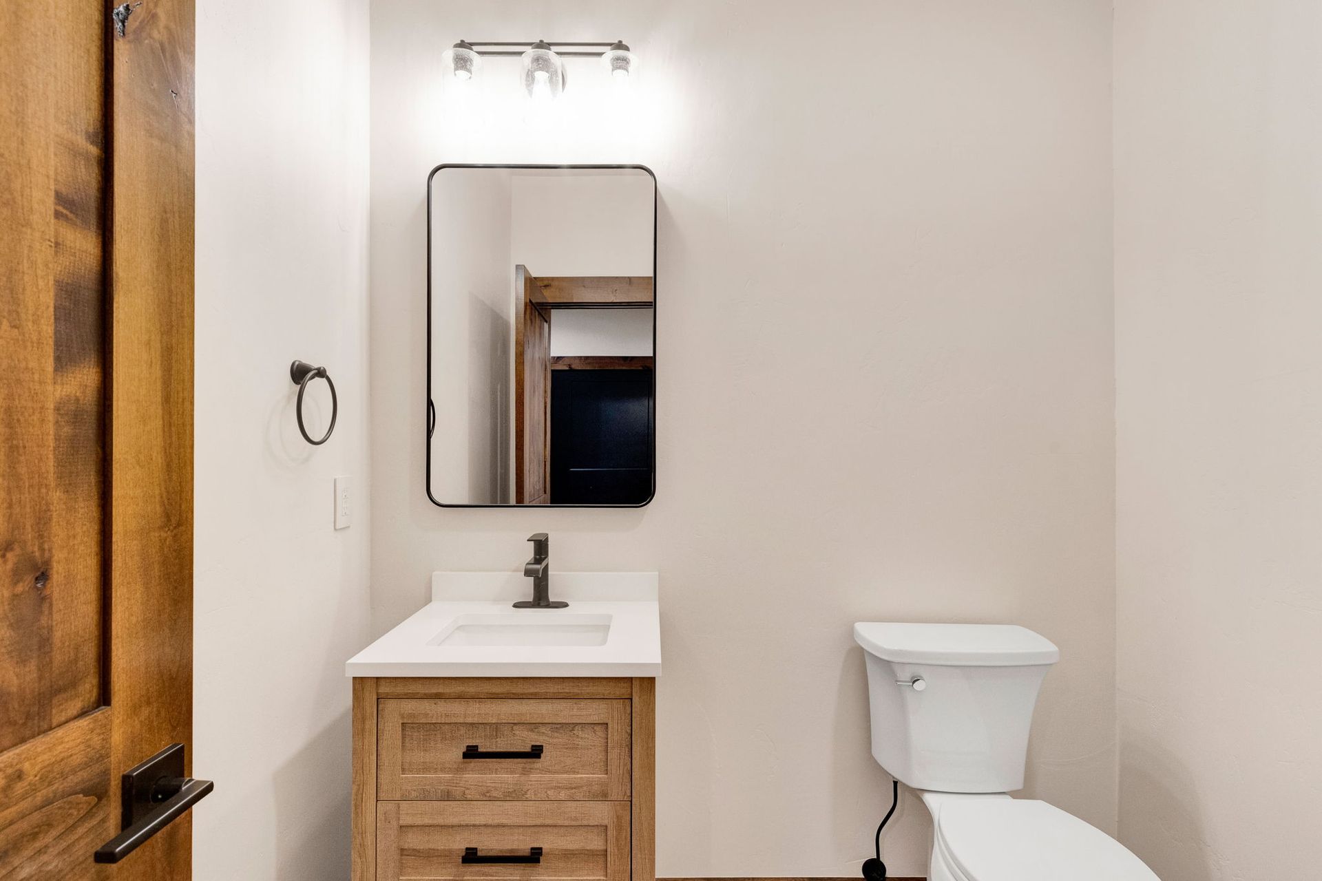 Small bathroom with wood vanity, mirror, sink, and toilet beside a wooden door.