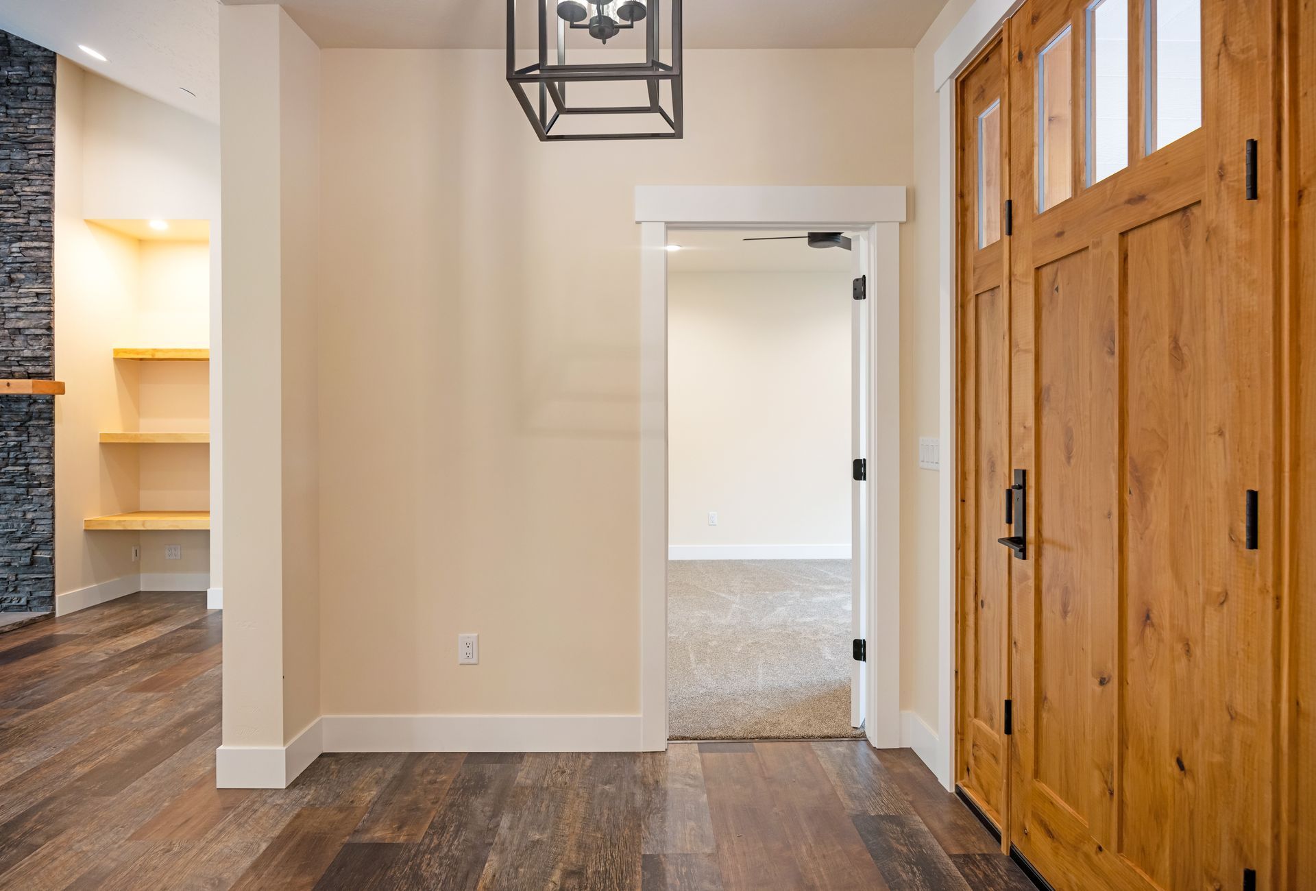 Entry hallway with wood floors, beige walls, hanging light, and double wooden doors; open doorway to another room