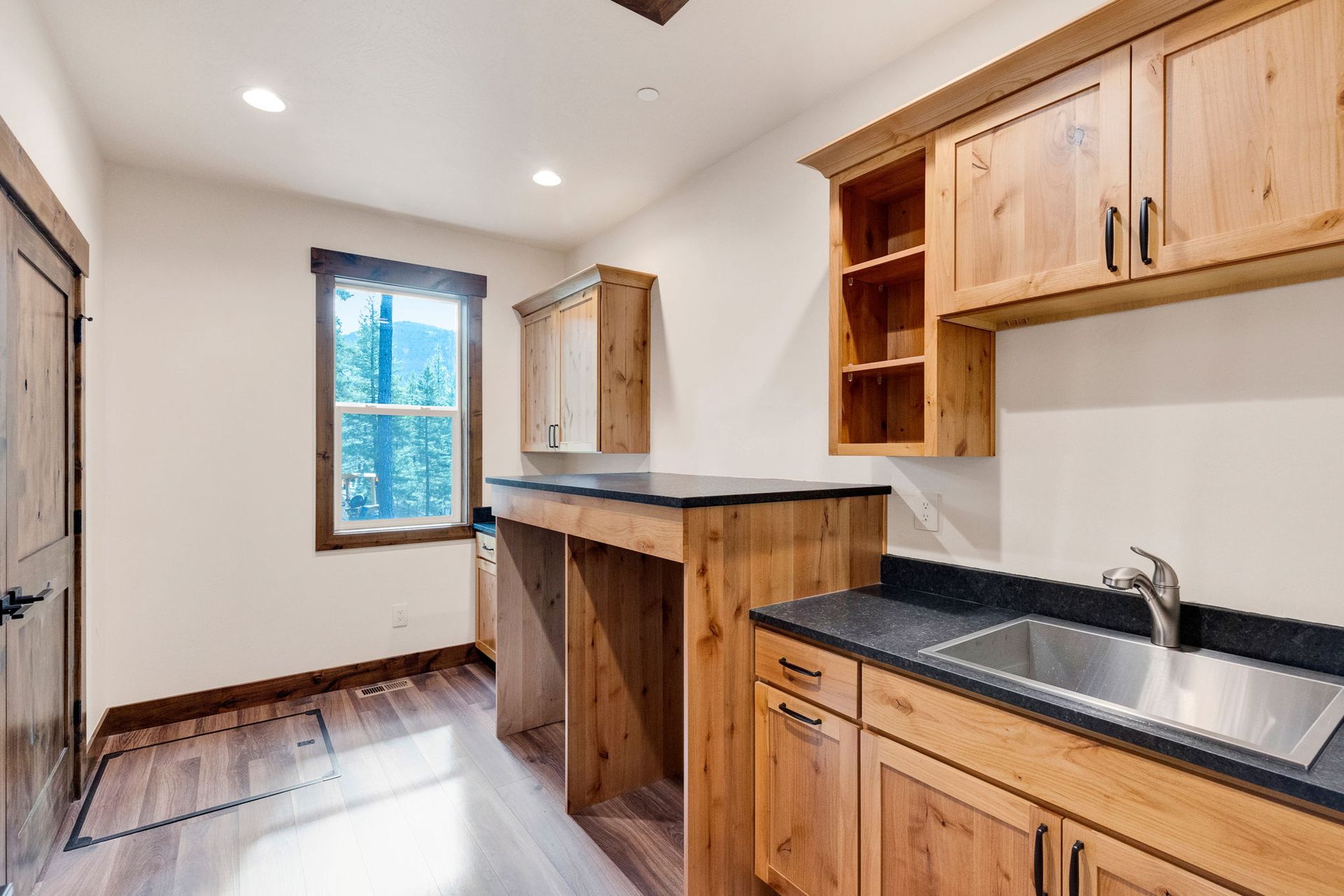 Narrow kitchen with wooden cabinets, black countertops, sink, and a window at the far end.