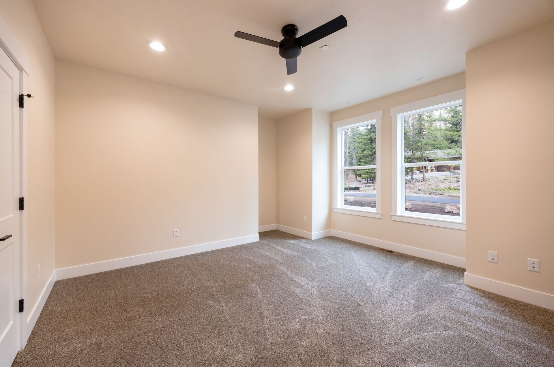 Empty beige bedroom with carpet, ceiling fan, and large windows.